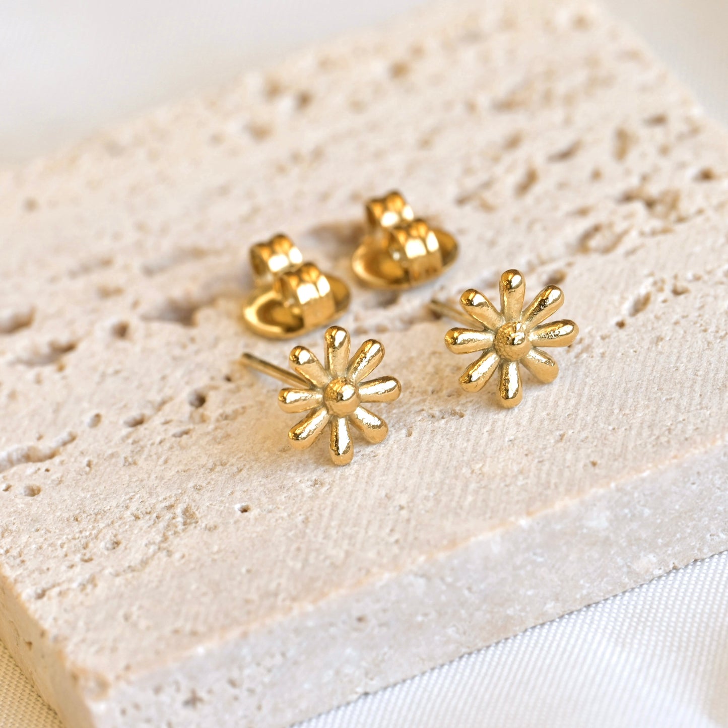 Gold floral earrings on a textured beige surface