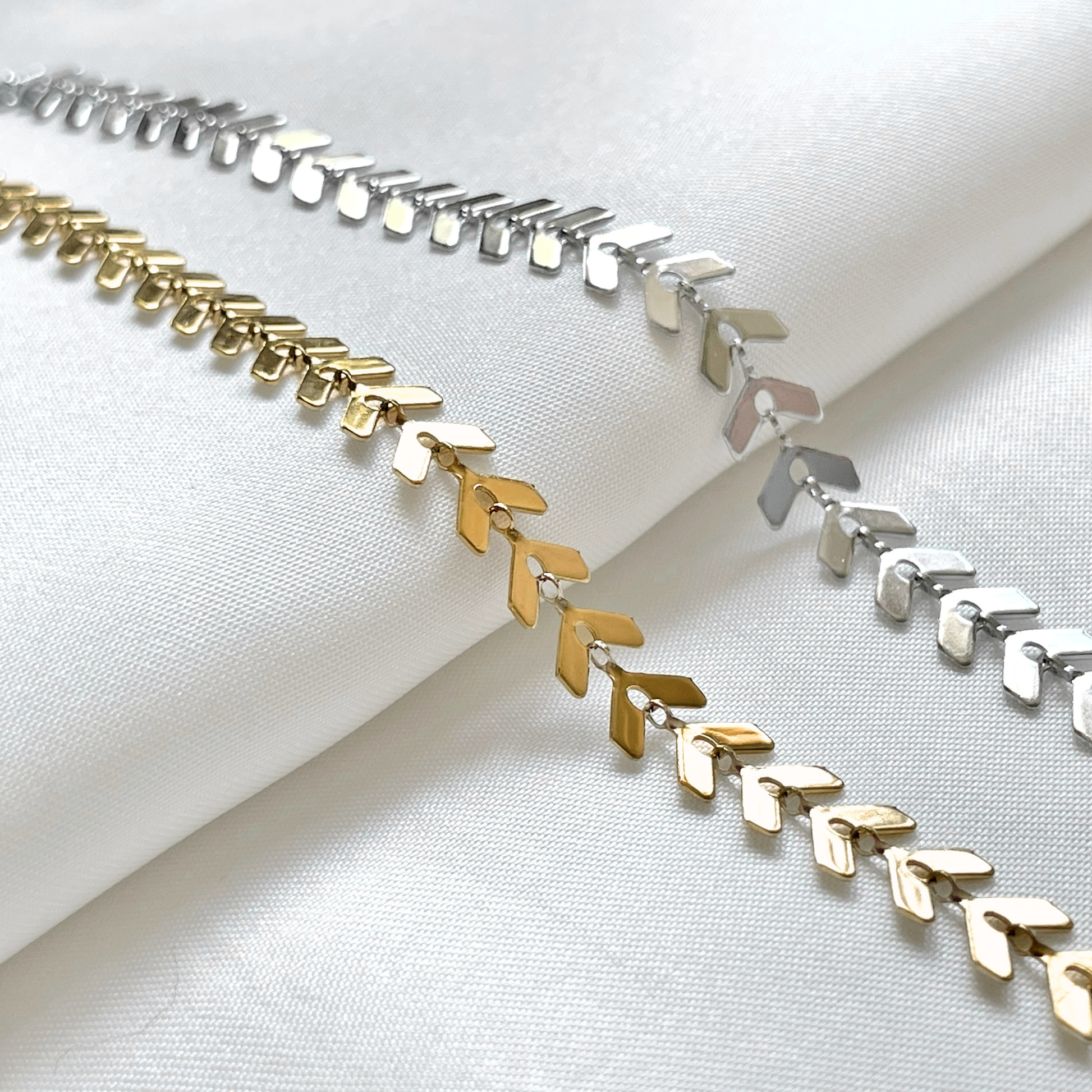 Two gold and silver chevron chains on a white fabric background