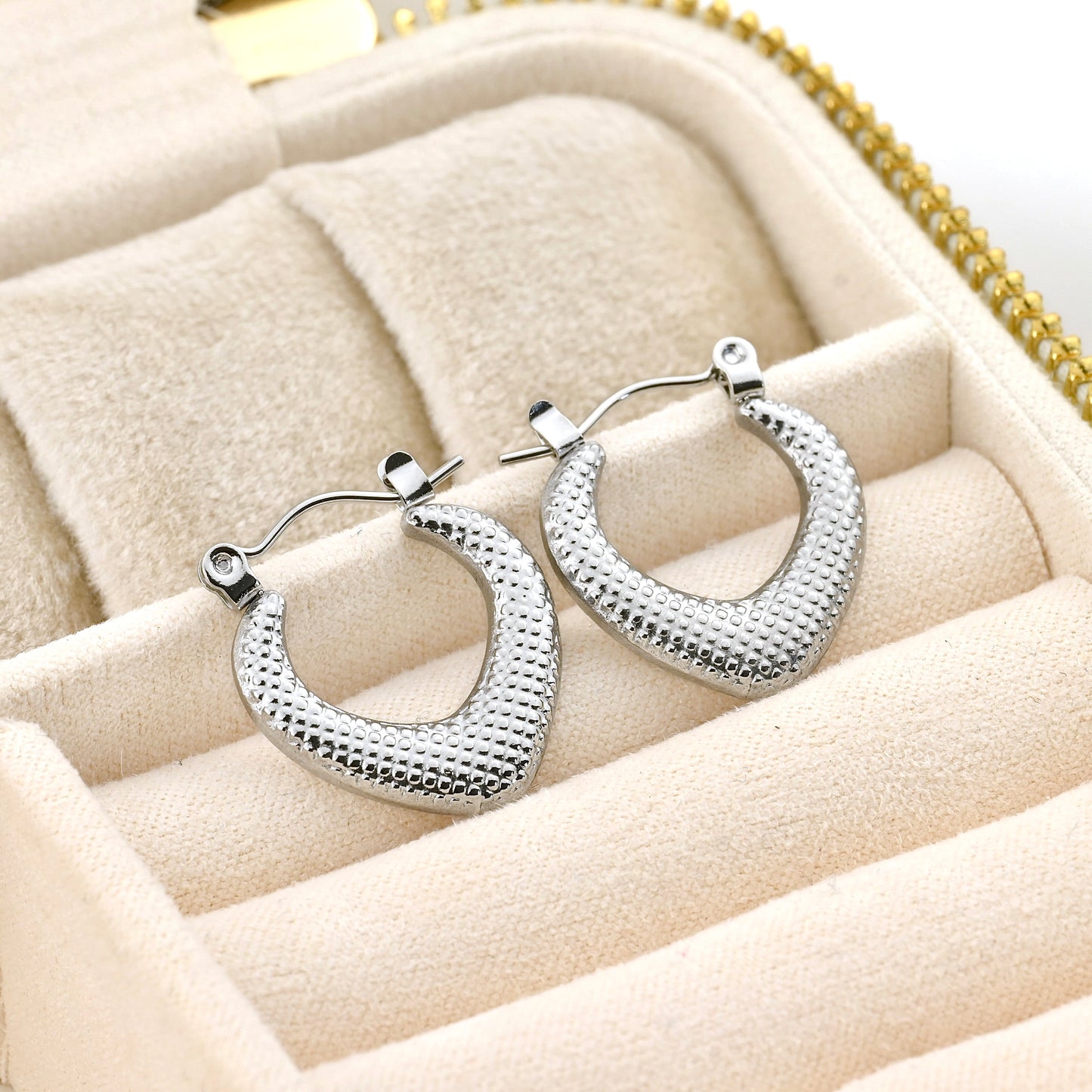 Textured silver rhombus hoop earrings on a soft beige surface
