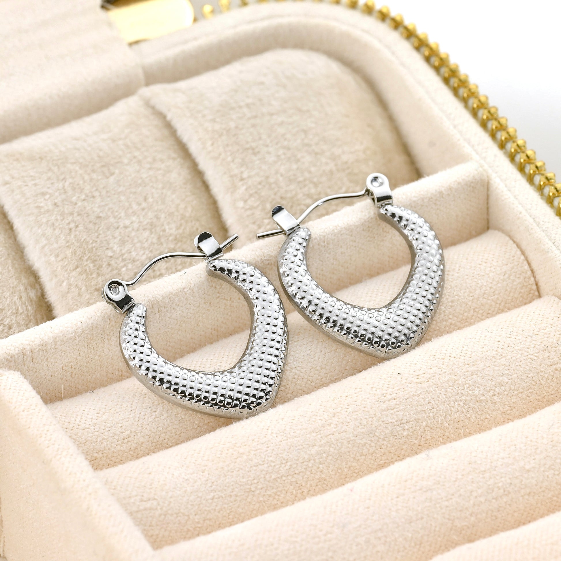 Textured silver rhombus hoop earrings on a soft beige surface