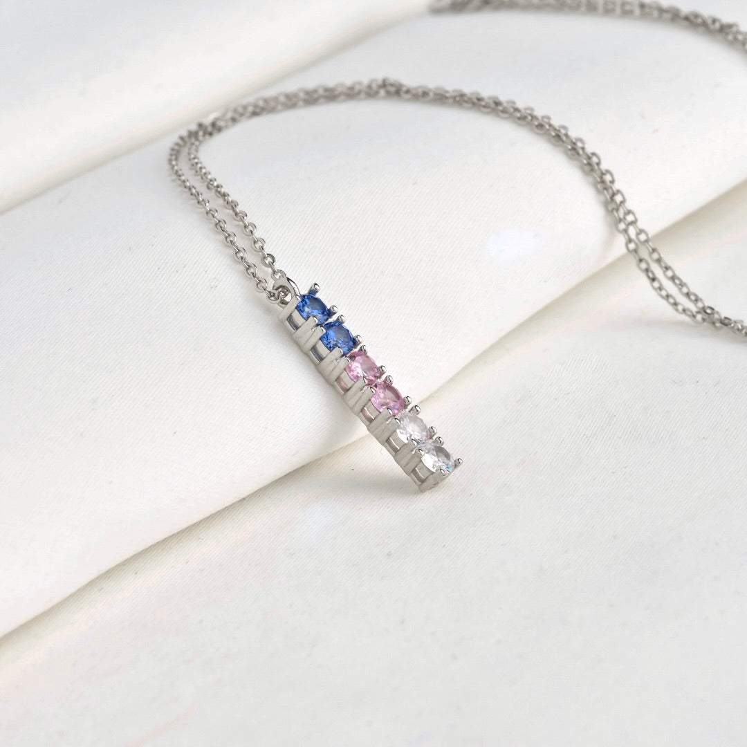 Silver necklace with a rectangular pendant featuring blue, pink, and clear gemstones on a white surface.