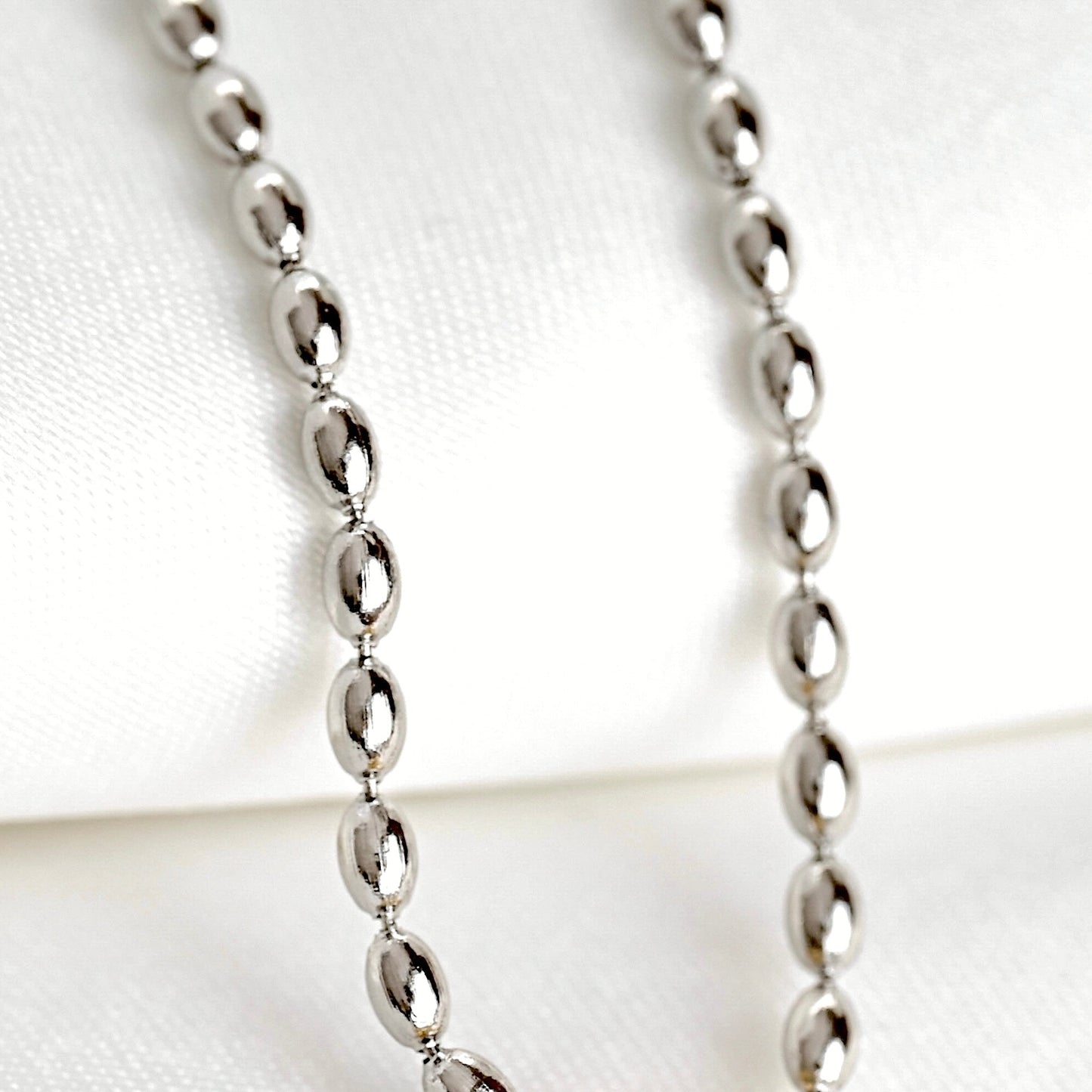 A silver beaded chain necklace with puffy oval links displayed on a soft white fabric background.