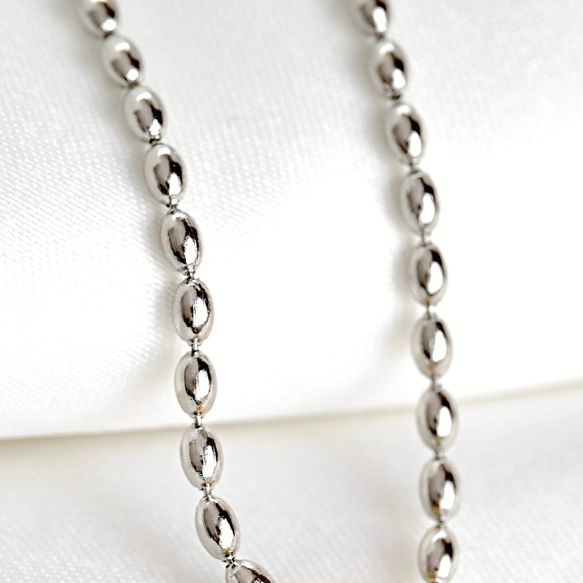 A silver beaded chain necklace with puffy oval links displayed on a soft white fabric background.