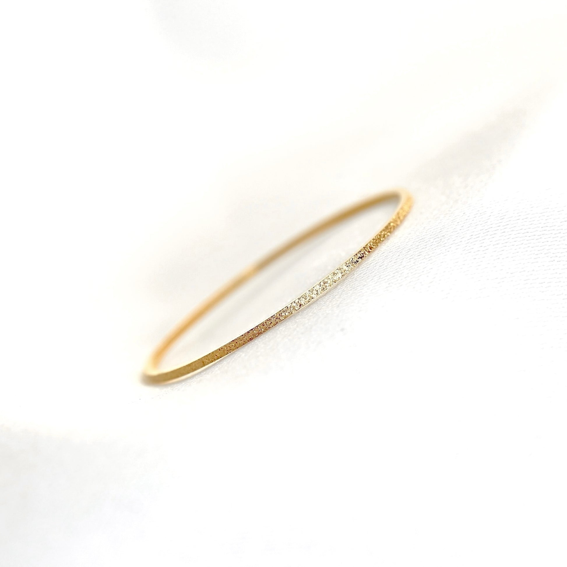A delicate gold ring with a textured finish displayed on a soft white fabric background.