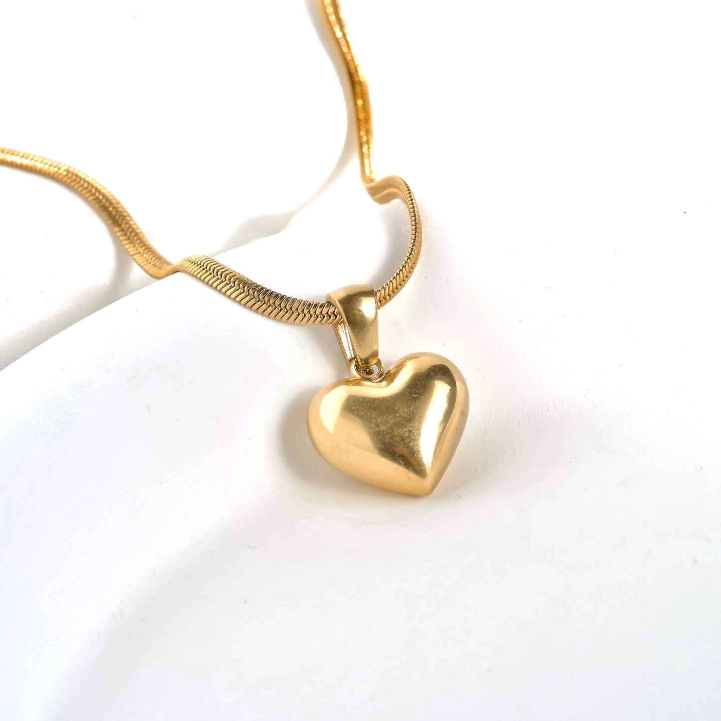 Gold herringbone necklace with a puffy heart charm on a white background
