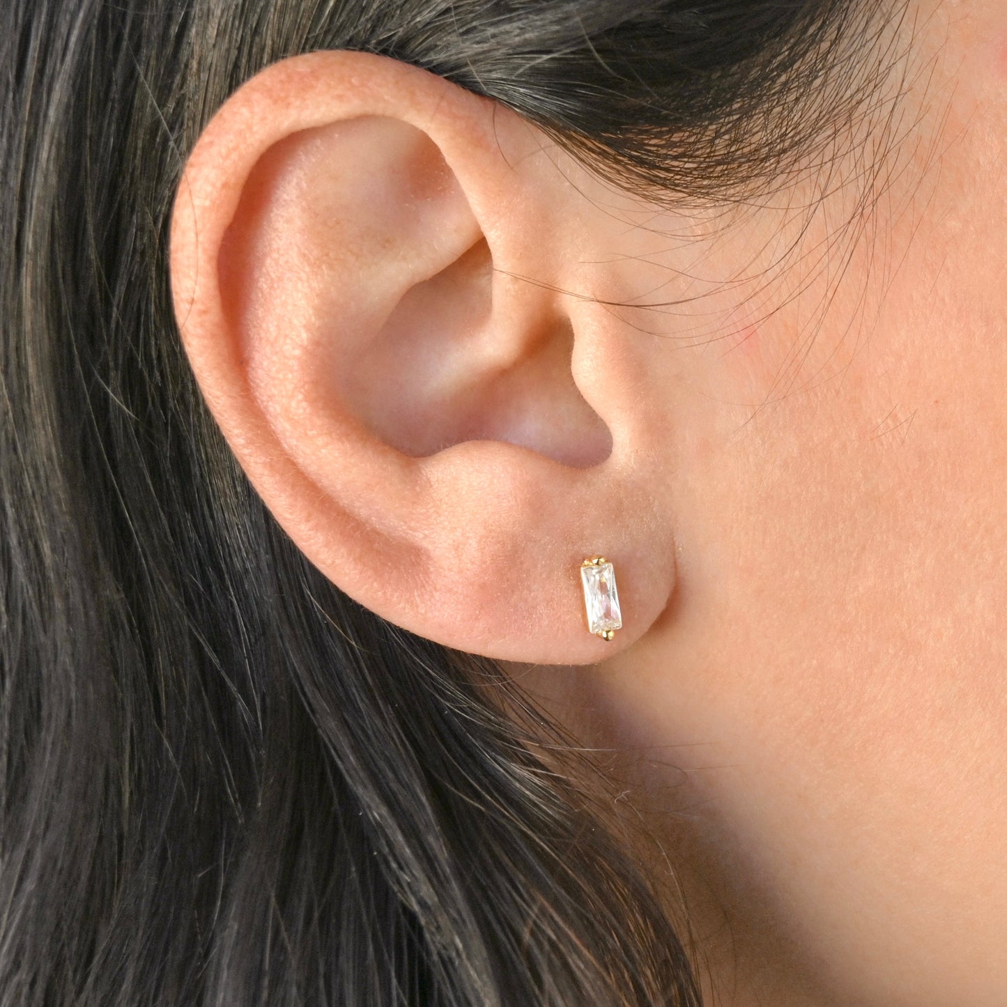 Close-up of an ear wearing a gold earring with a clear gemstone.