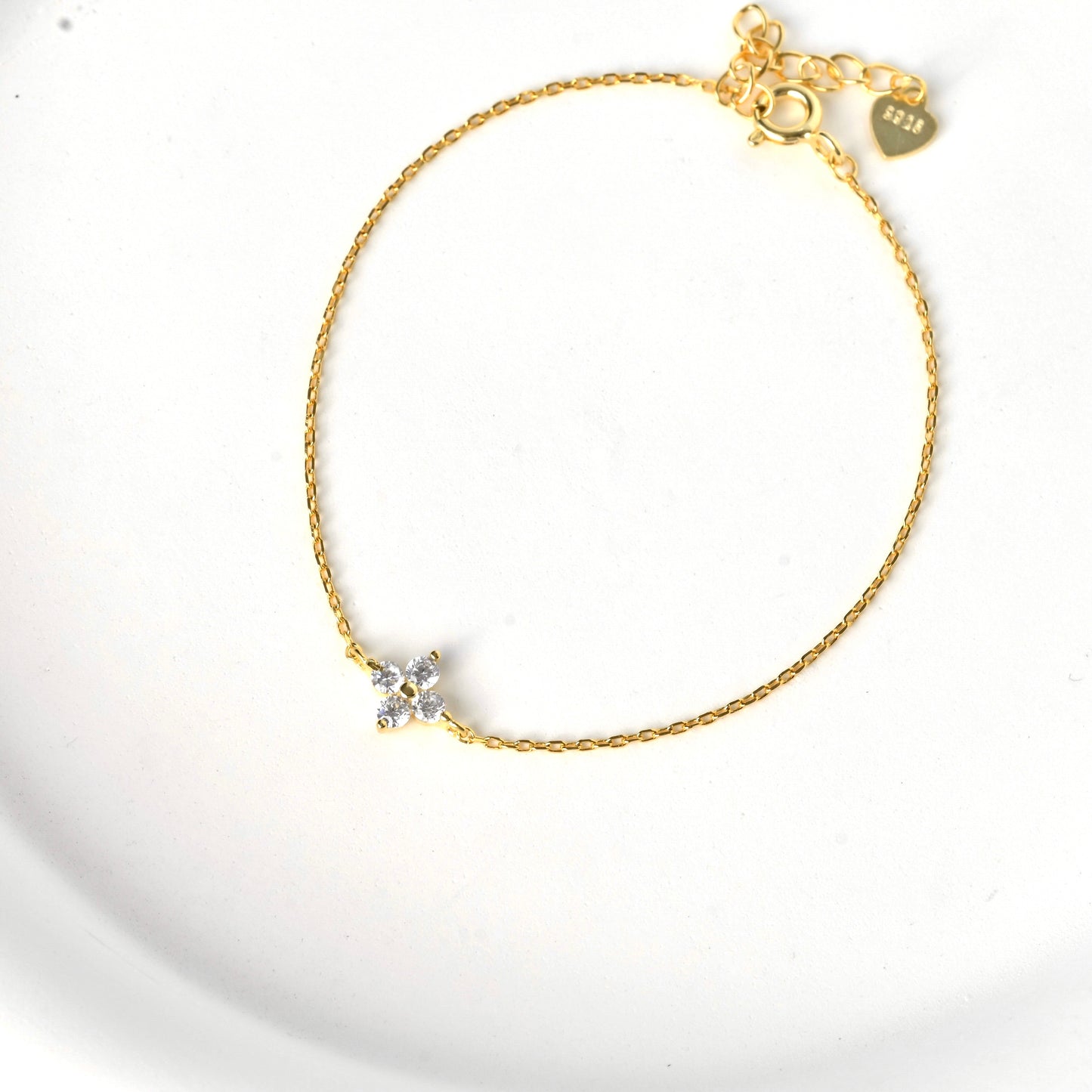Top view of gold cz clover bracelet with a spring ring clasp and an S925 stamped heart charm at the end of extender chain on a white background