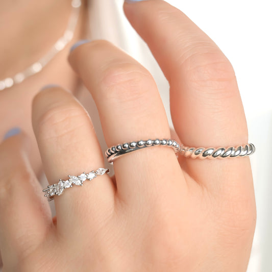 Close-up of a hand wearing three silver rings, one with marquise CZ, one mixed texture entwined and one thin twisted croissant, on a white background