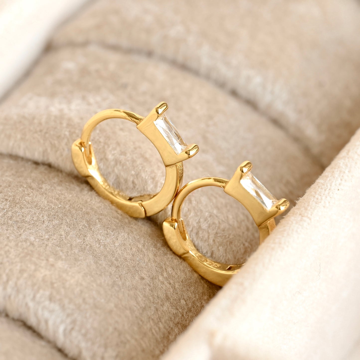 Gold hoop earrings with a central gemstone on a beige fabric background