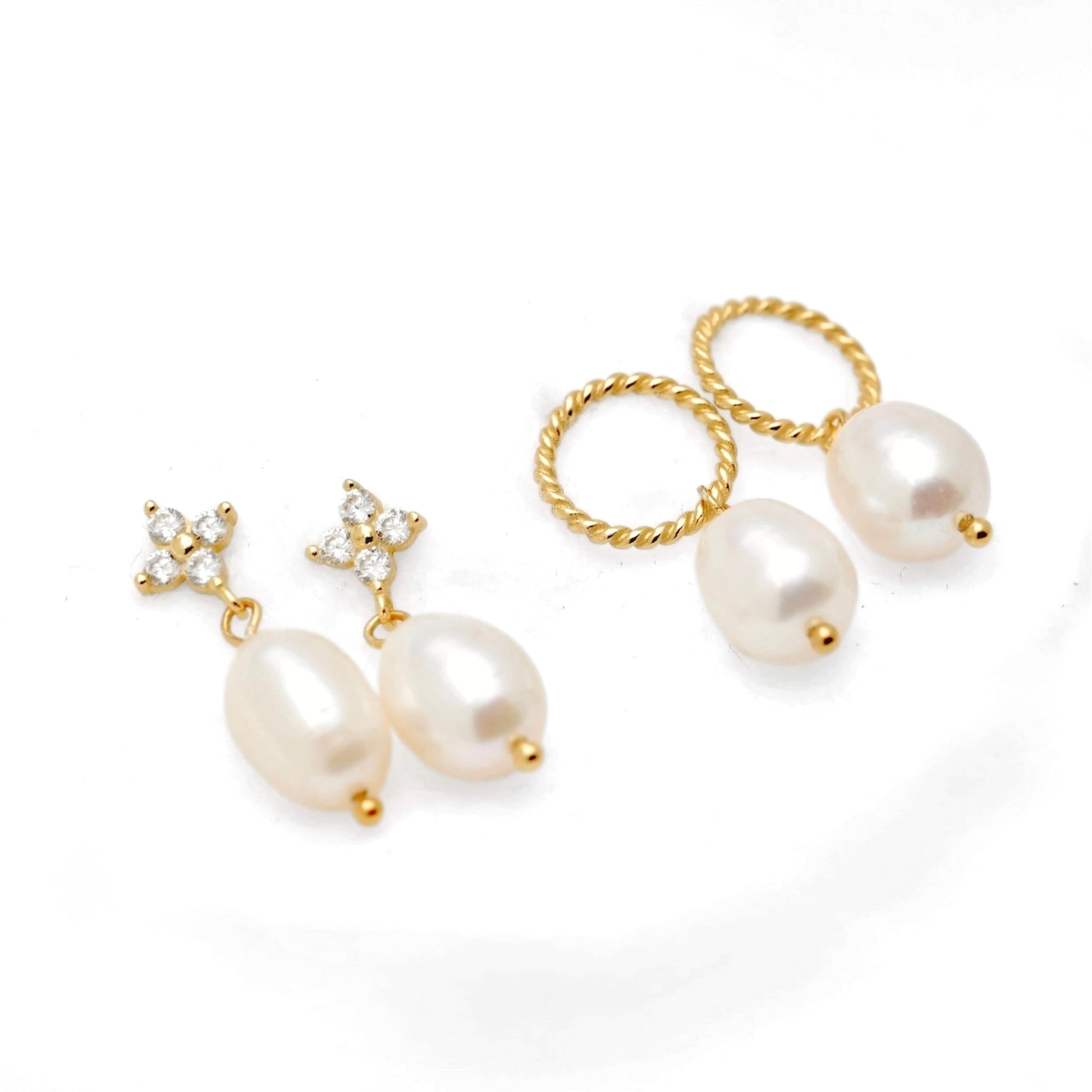 A pair of gold-tone drop earrings with large oval white pearls, shown alongside pearl earrings with twisted gold hoops on a clean white background.