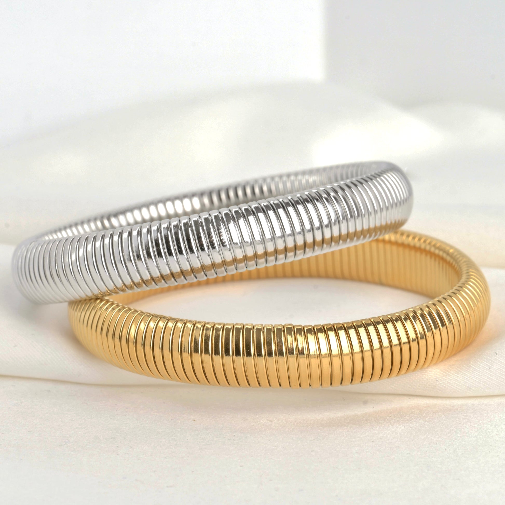 Two metallic bangles, one gold and one silver,  stacked on a light background.