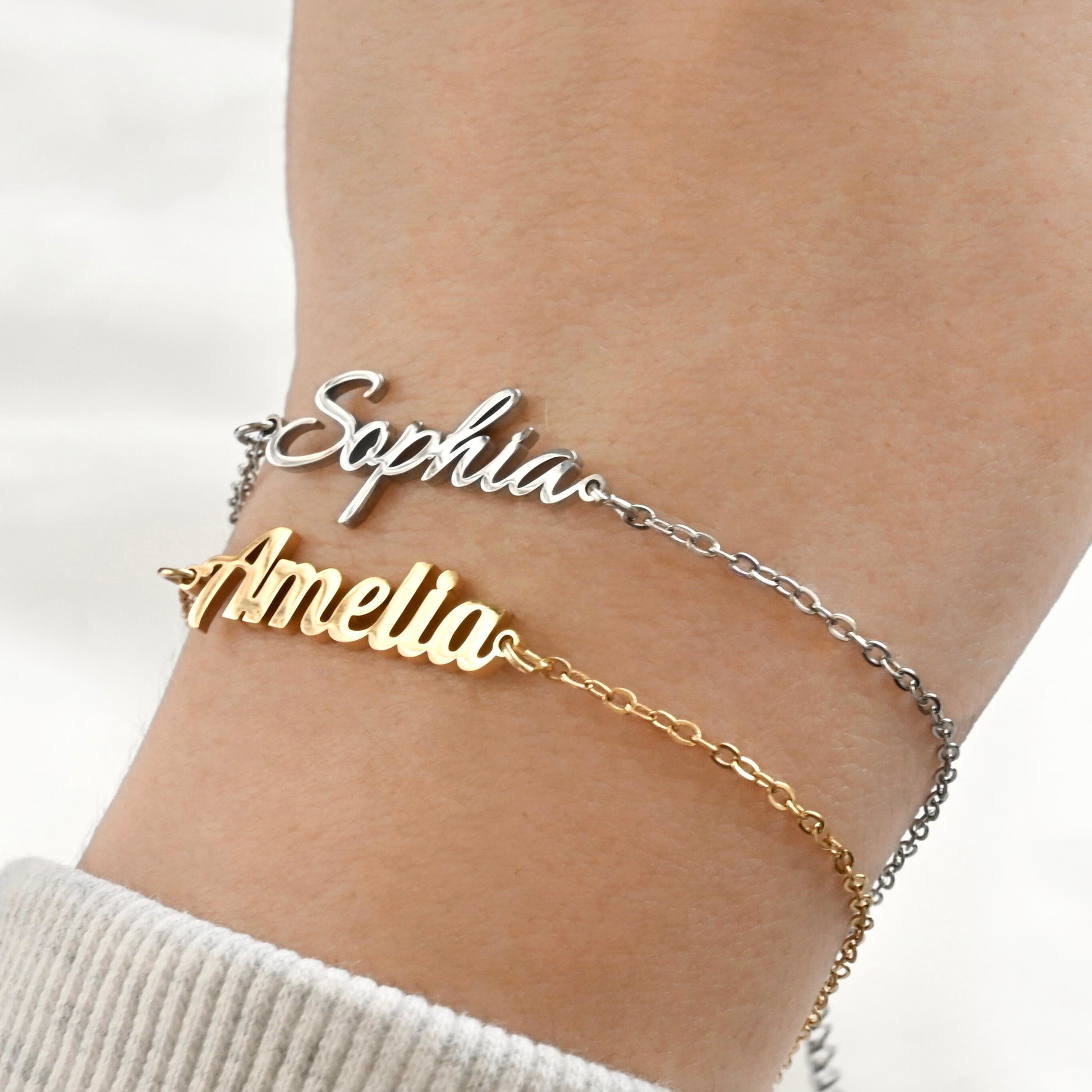 Gold and silver name bracelets on a wrist against a white background