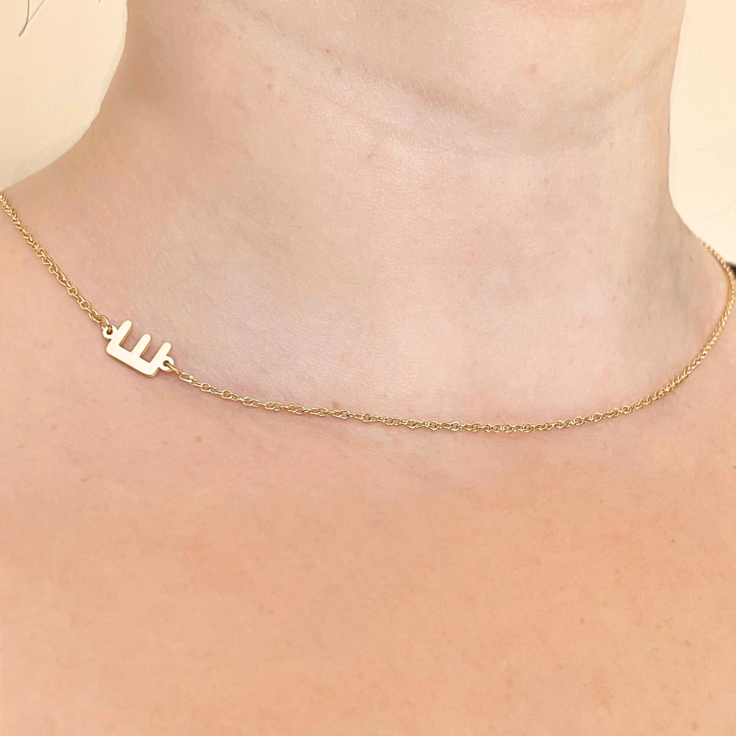 Person wearing a gold necklace with an upper-case letter 'E' placed sideways on a cable chain 