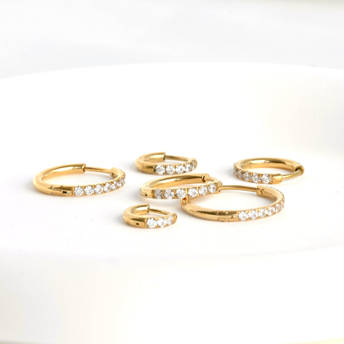 Set of gold hoop earrings with clear stones on a white background