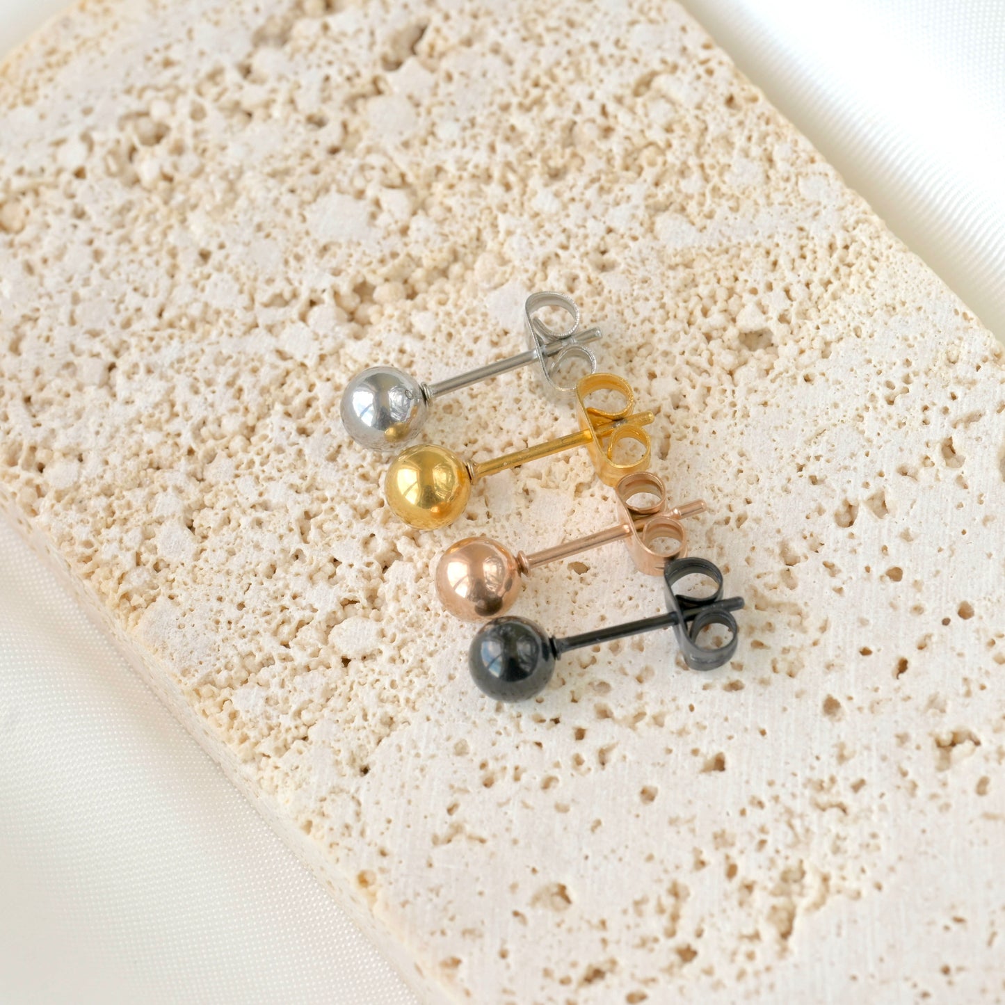 Top view of set of small round stud earrings in various colors on a textured beige surface