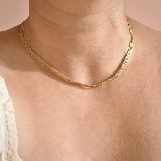 Gold mesh chain necklace on a person against a neutral background