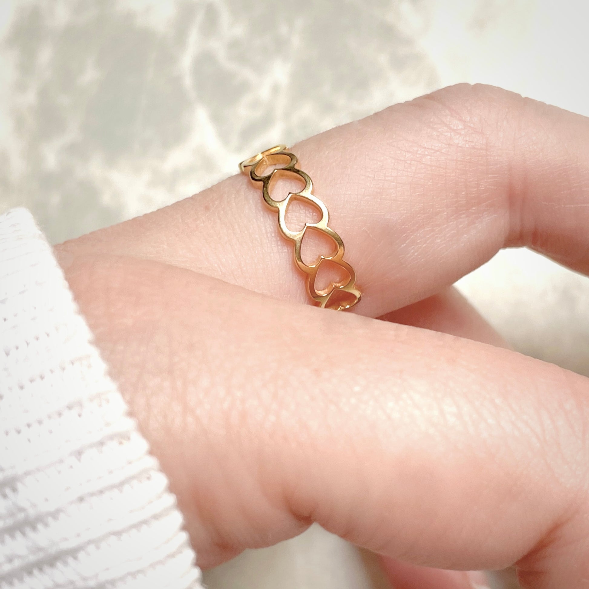 Dainty gold  heart chain ring on a finger with a soft white background