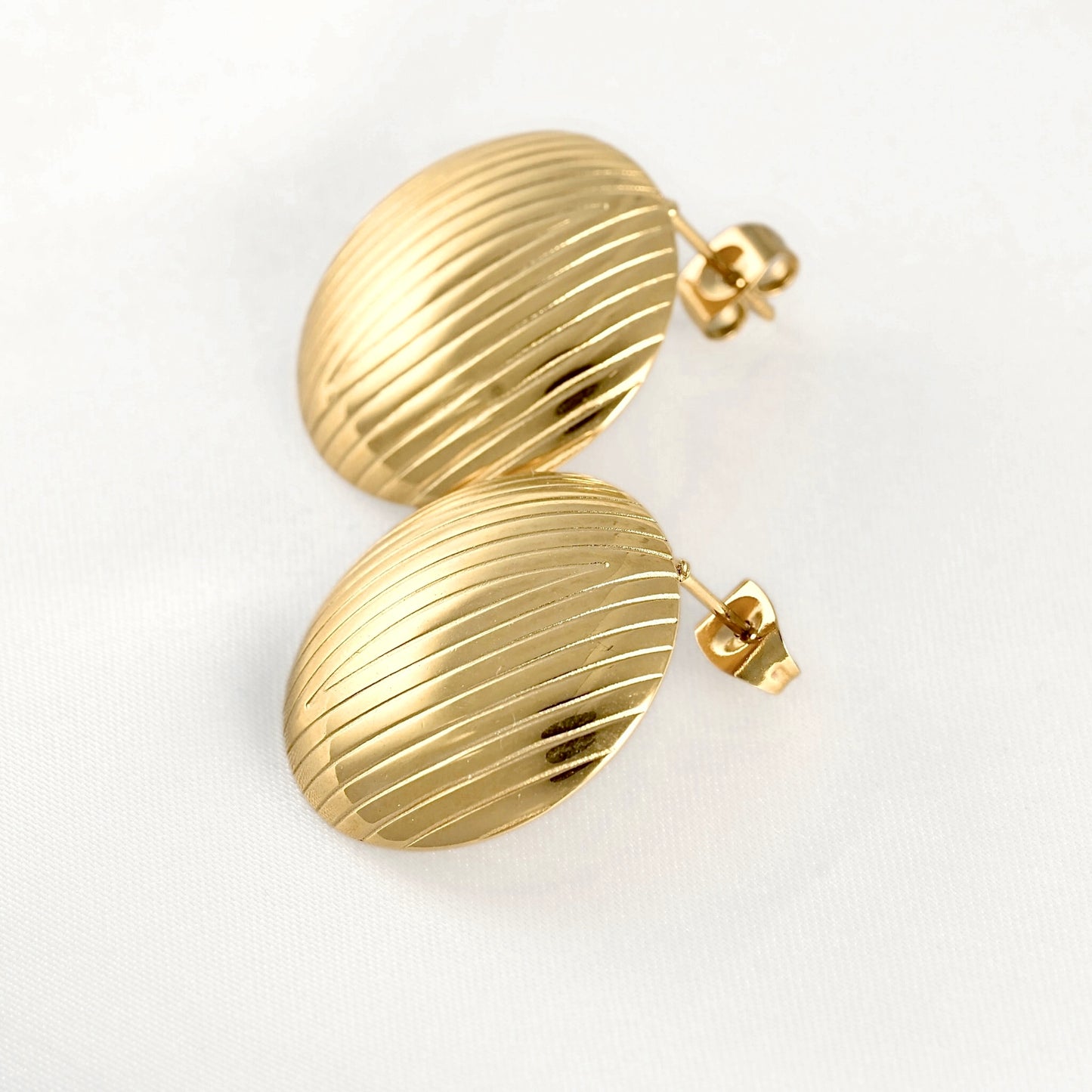 A pair of gold oval stud earrings with a ribbed, textured surface, displayed on a clean white background.