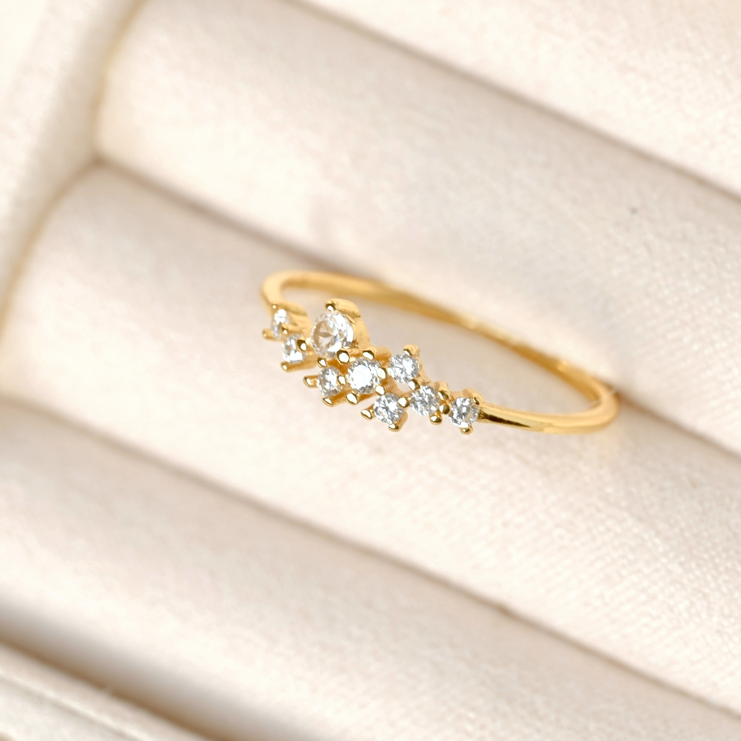 A delicate gold ring featuring a cluster of clear marquise-cut gemstones, displayed on a cream-colored textured jewelry box.