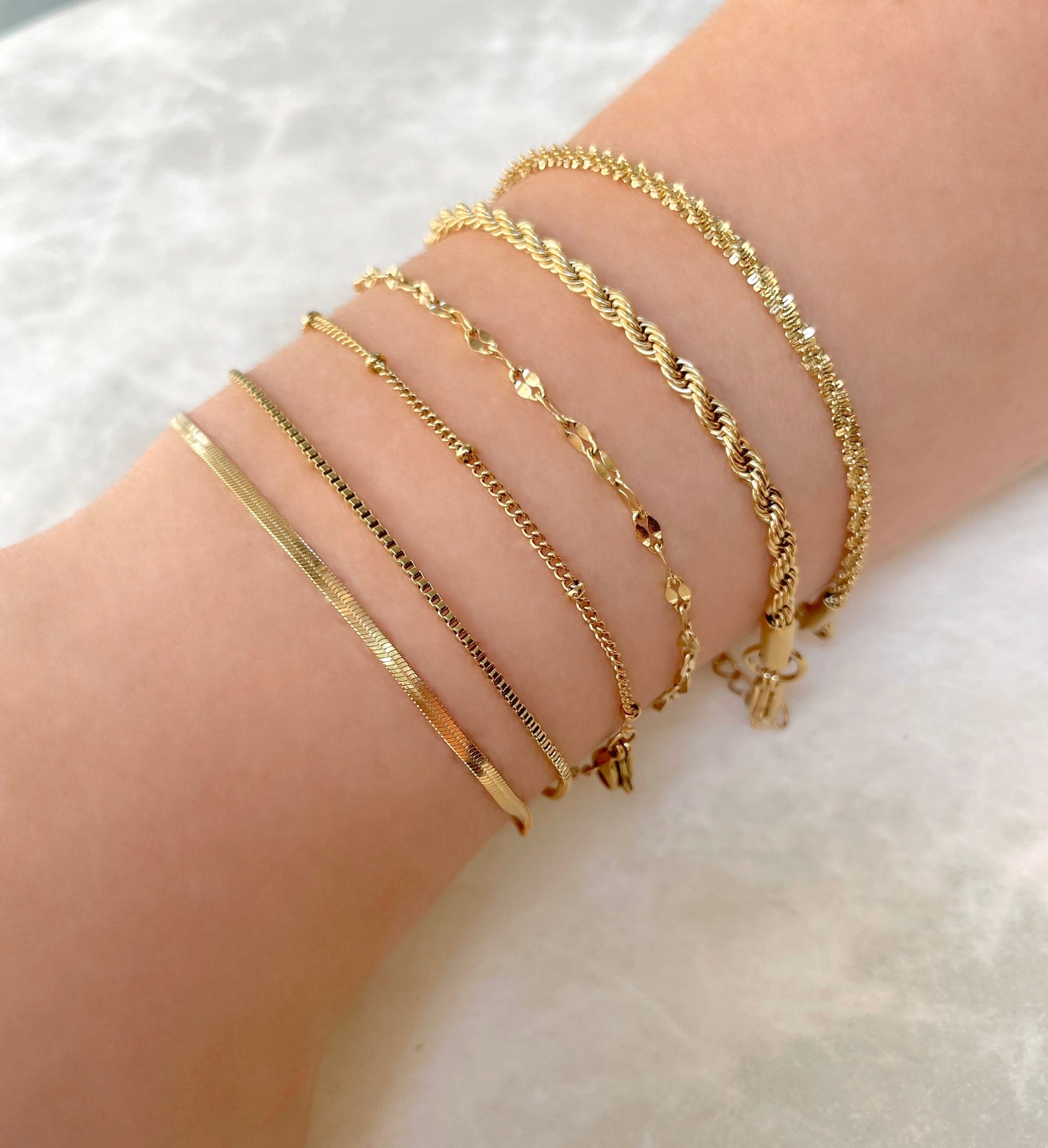 Gold bracelets on a person's wrist against a white background