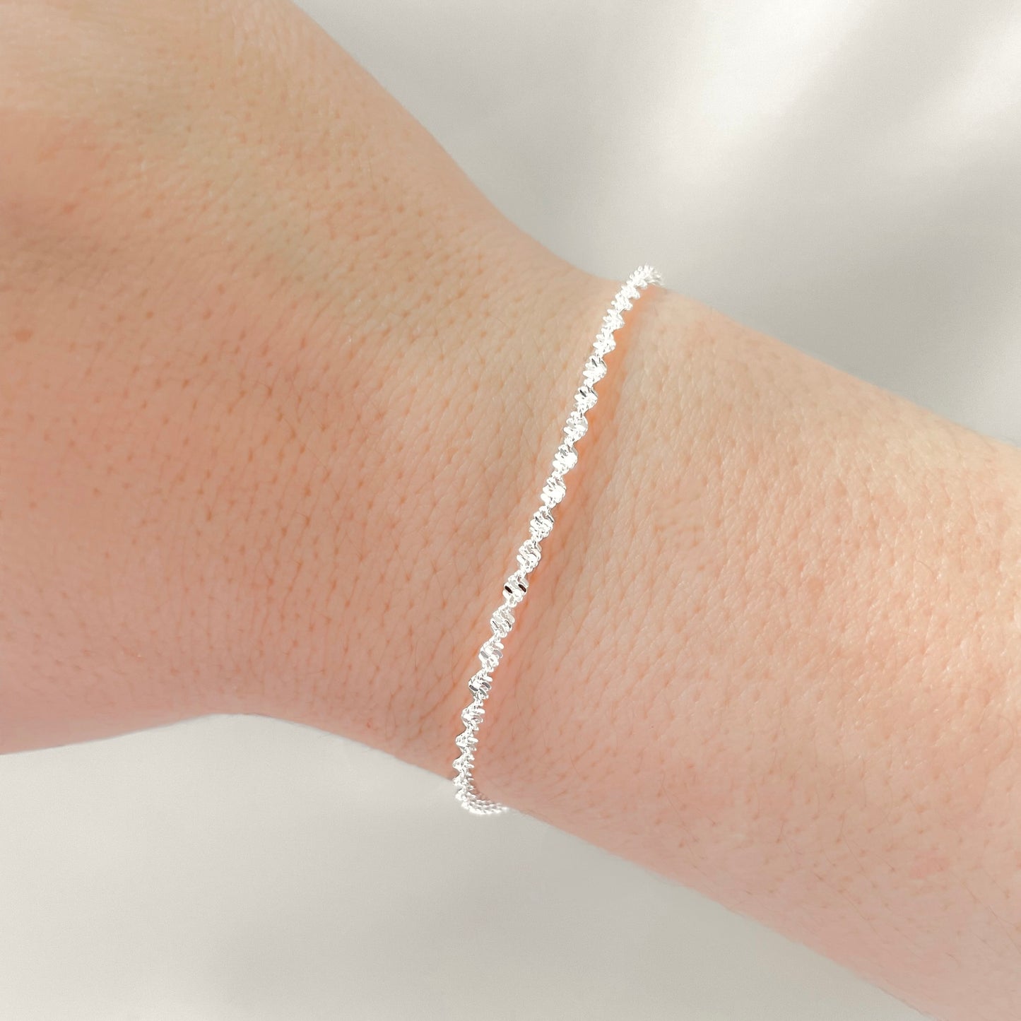 Silver twisted chain bracelet on a person's wrist against a neutral background