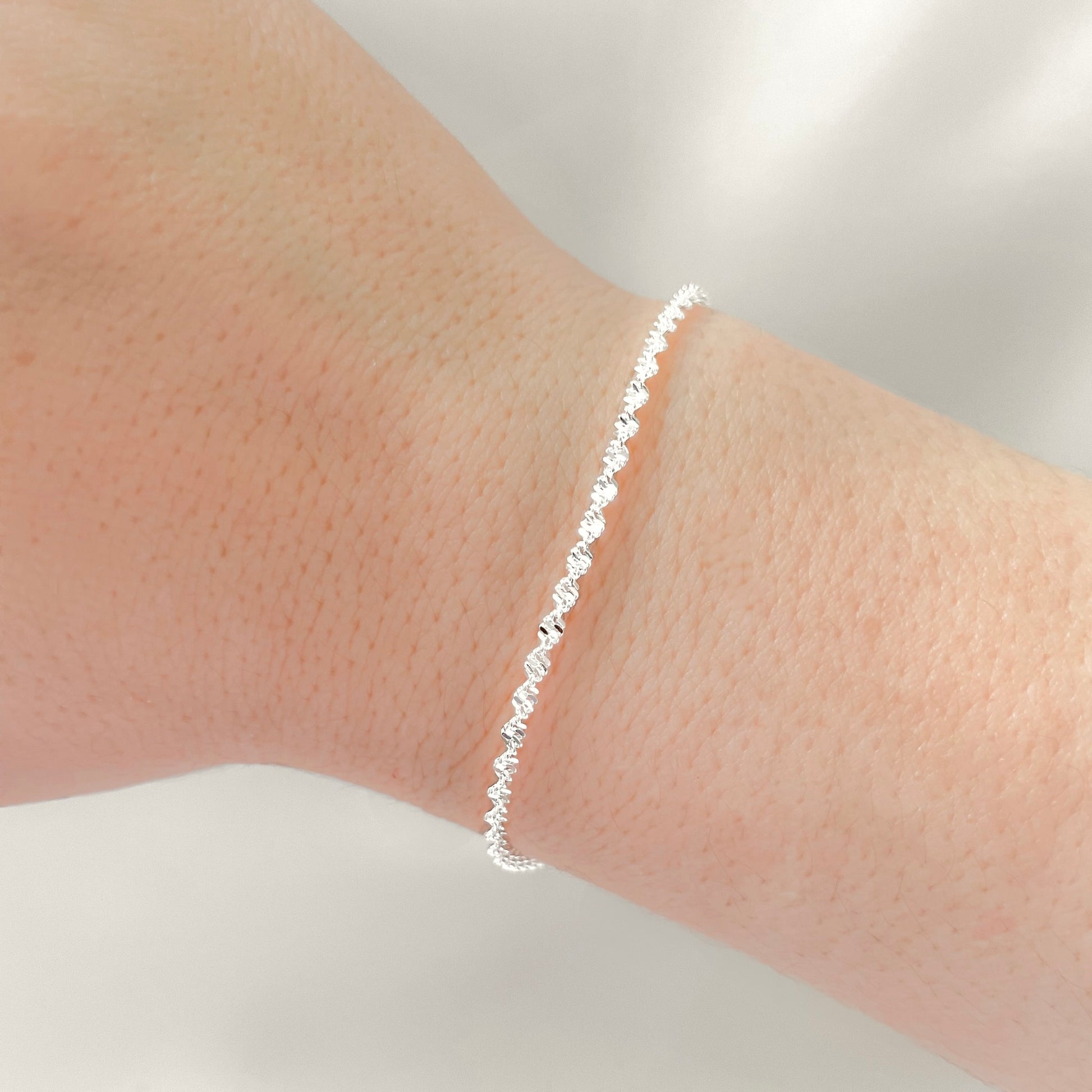Silver twisted chain bracelet on a person's wrist against a neutral background