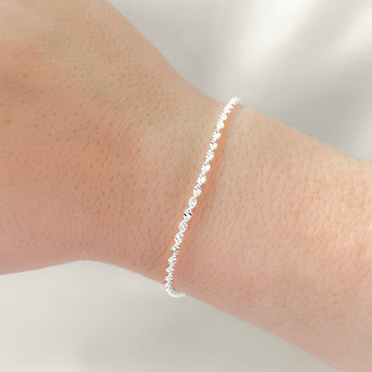 Silver twisted chain bracelet on a person's wrist against a neutral background