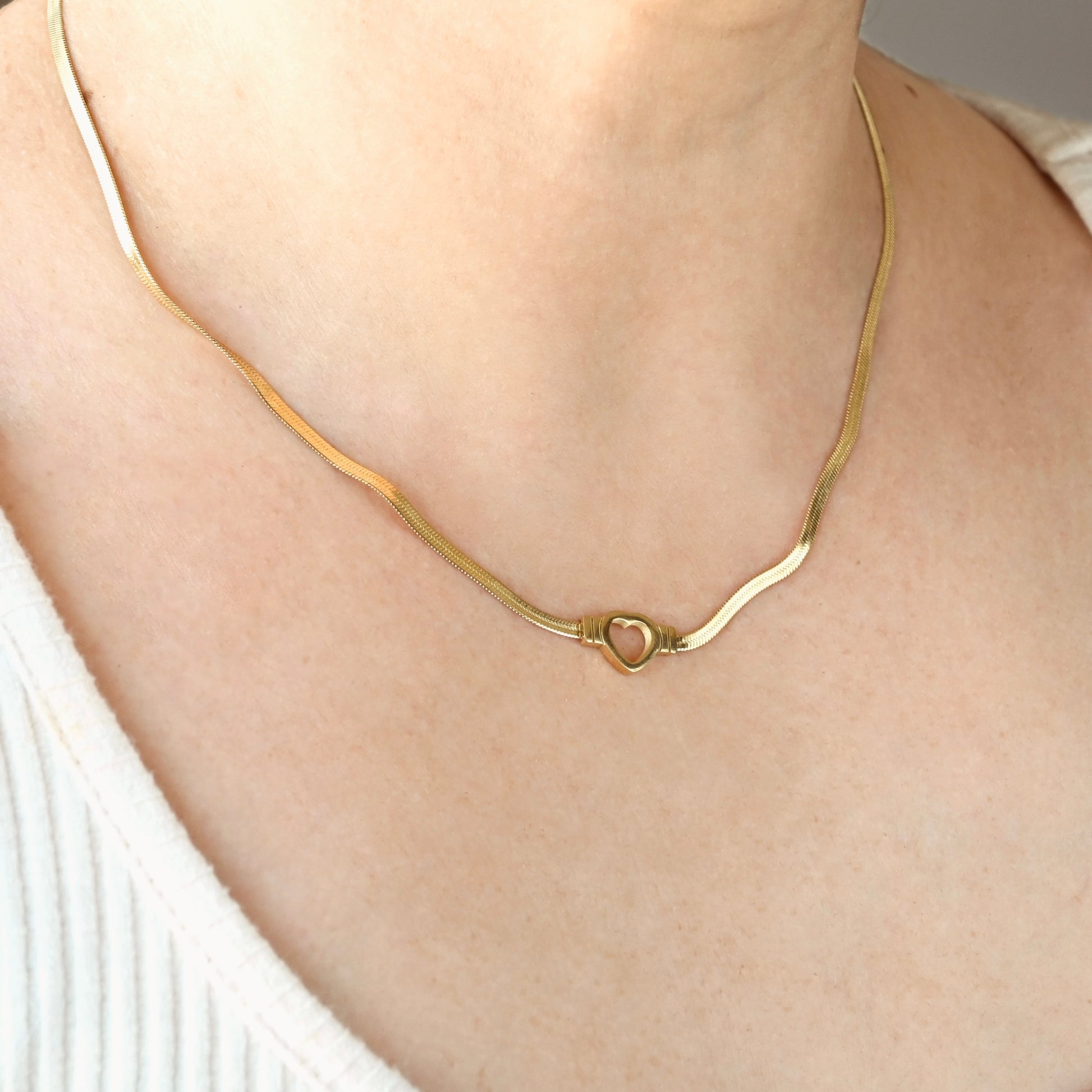Gold necklace with a heart charm worn by a person