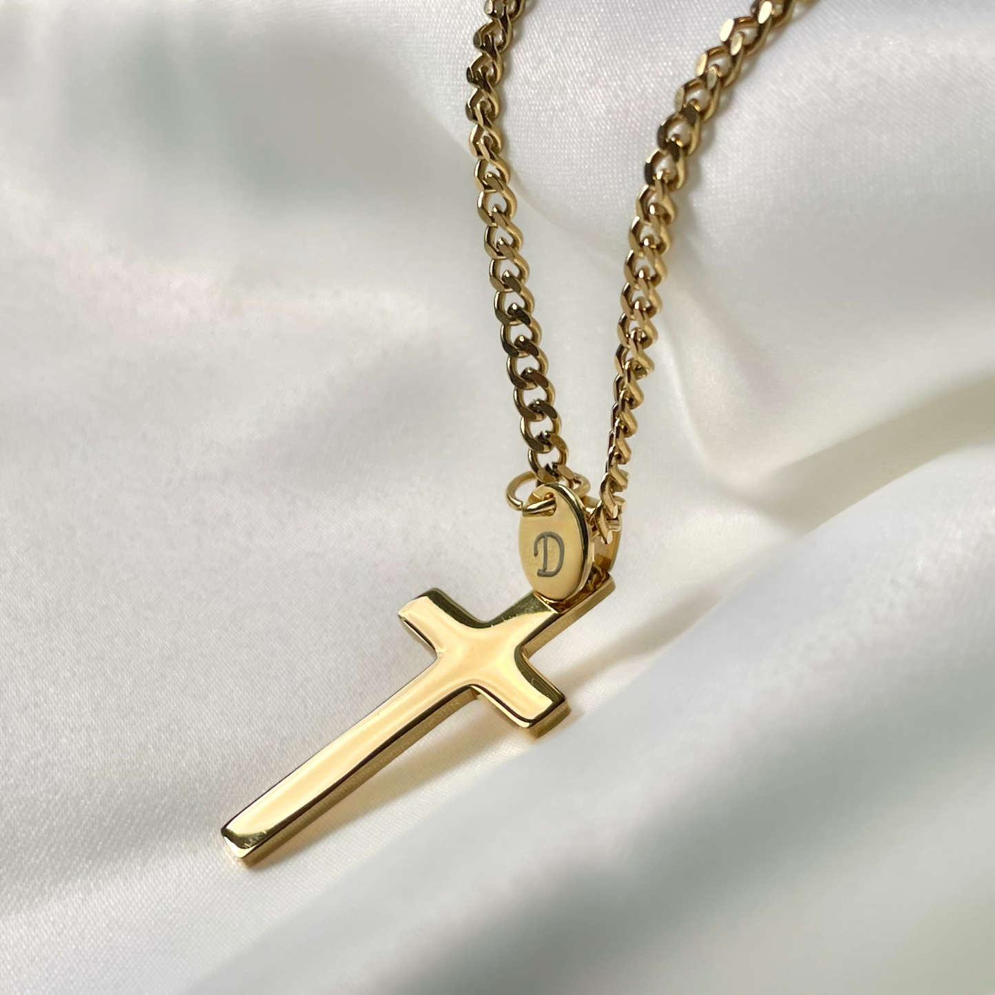 Gold necklace with a high-polish cross pendant on a white fabric background