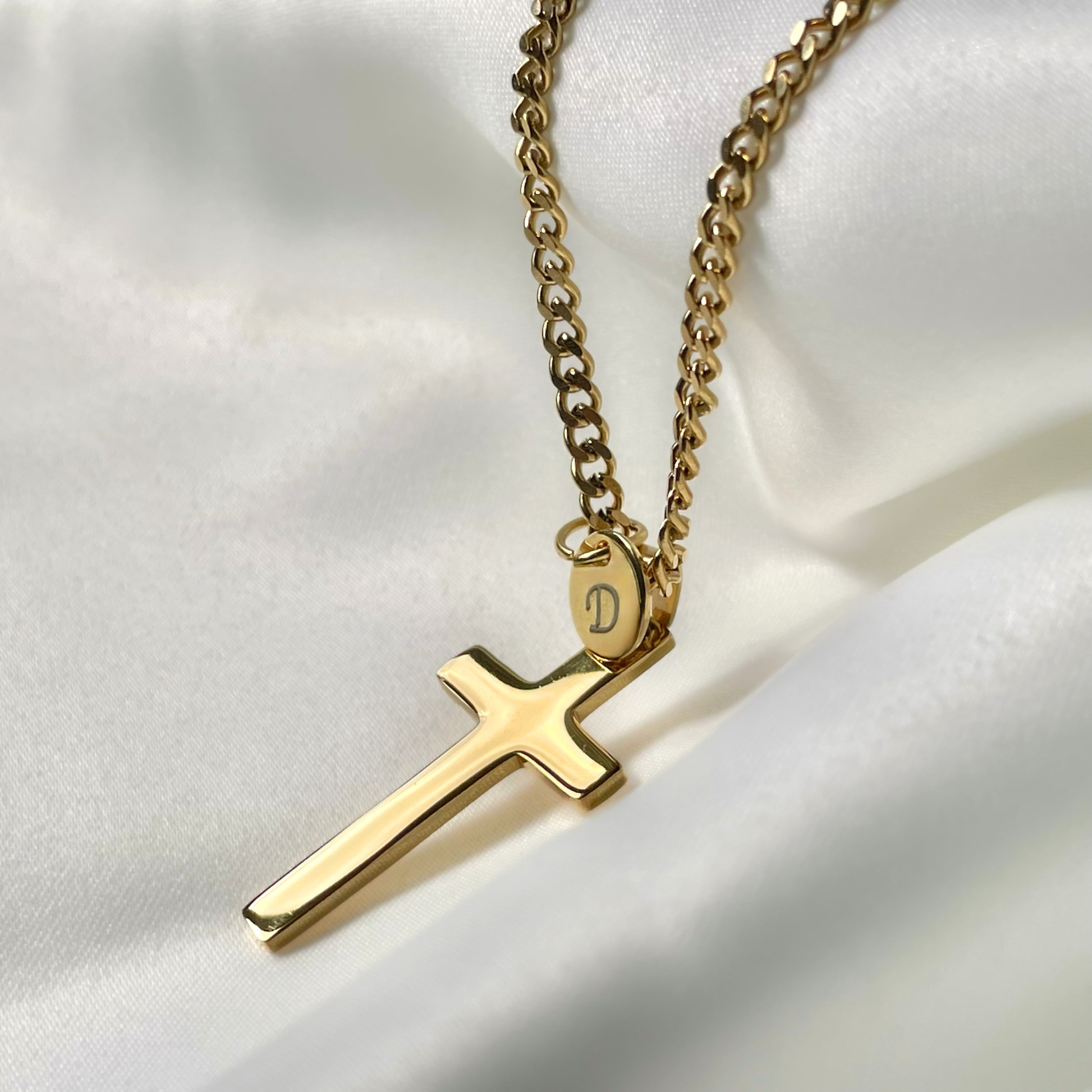 Gold necklace with a high-polish cross pendant on a white fabric background