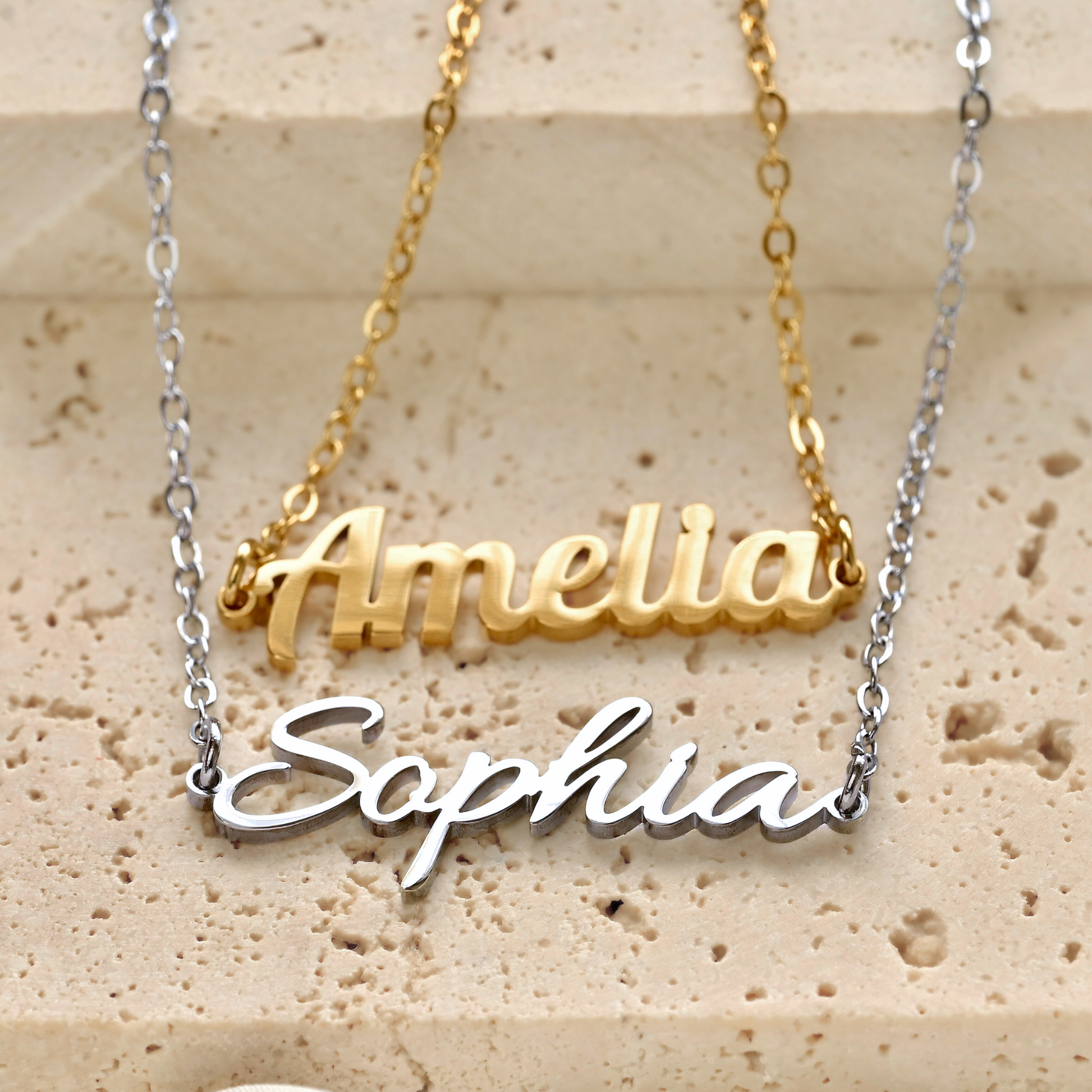 Gold and silver name necklaces on a textured beige surface