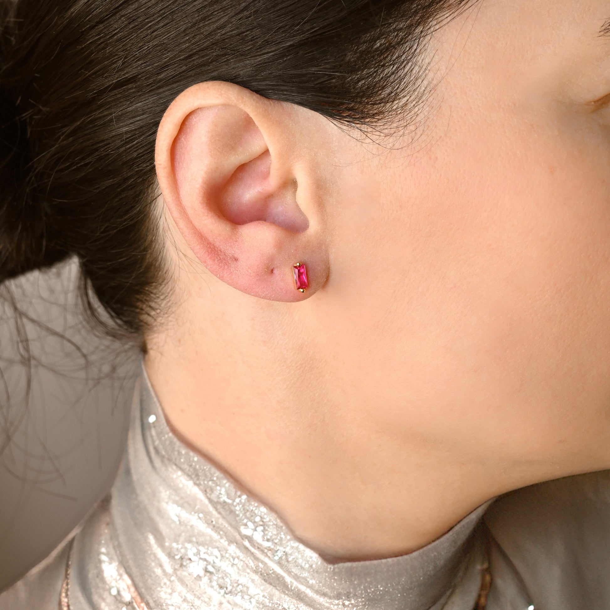 Close-up of an ear wearing a ruby stud earring with a neutral background