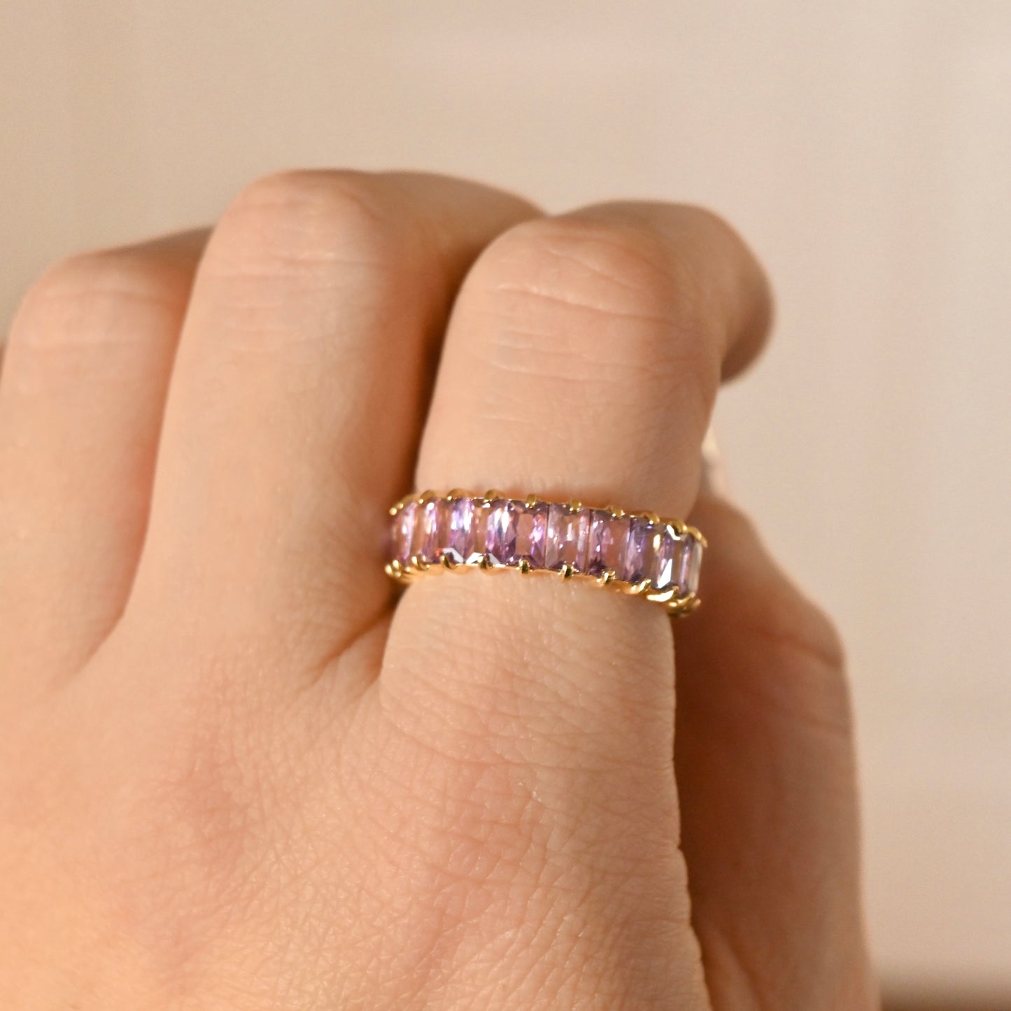 Gold ring with june birthstone on a person's finger against a beige background