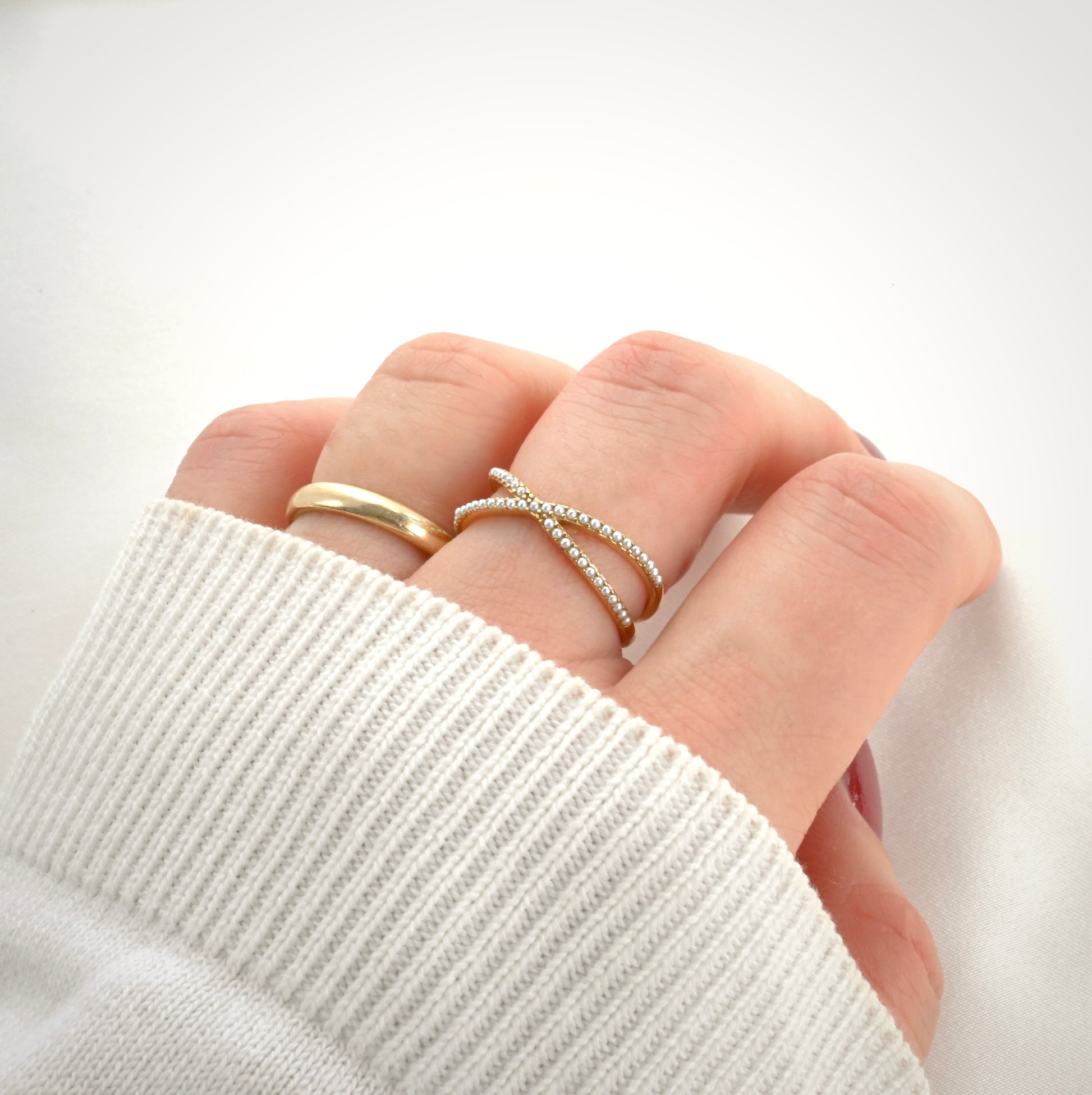Hand wearing an X-shaped half eternity pearl ring against a white background