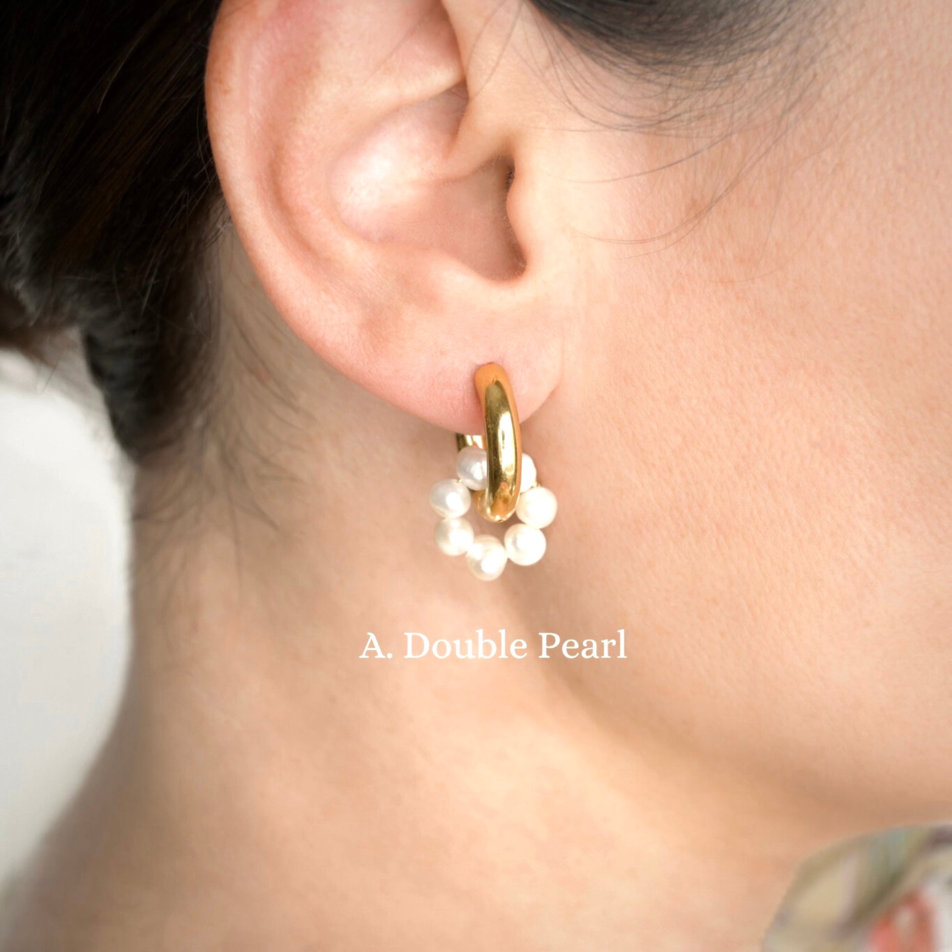 Gold hoop earring with white pearl charm circle worn by a person