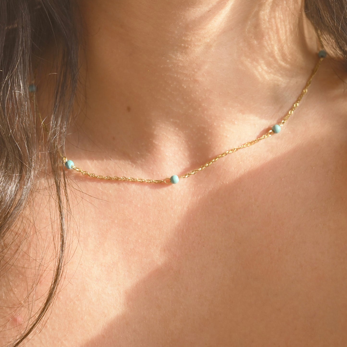 Close-up of a gold necklace with turquoise beads on a person's neck.