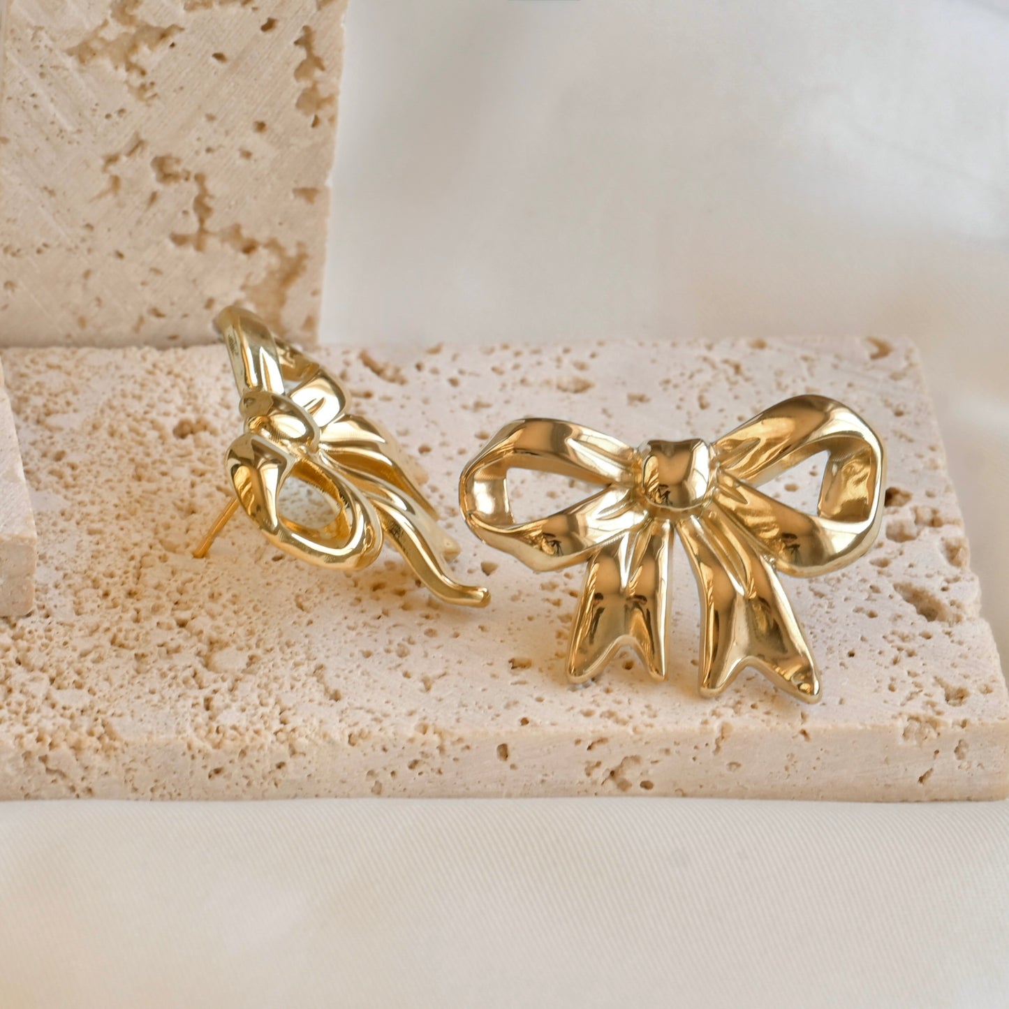 Close up of fluid ribbon earrings, one front view, one side view, on a textured stone surface view