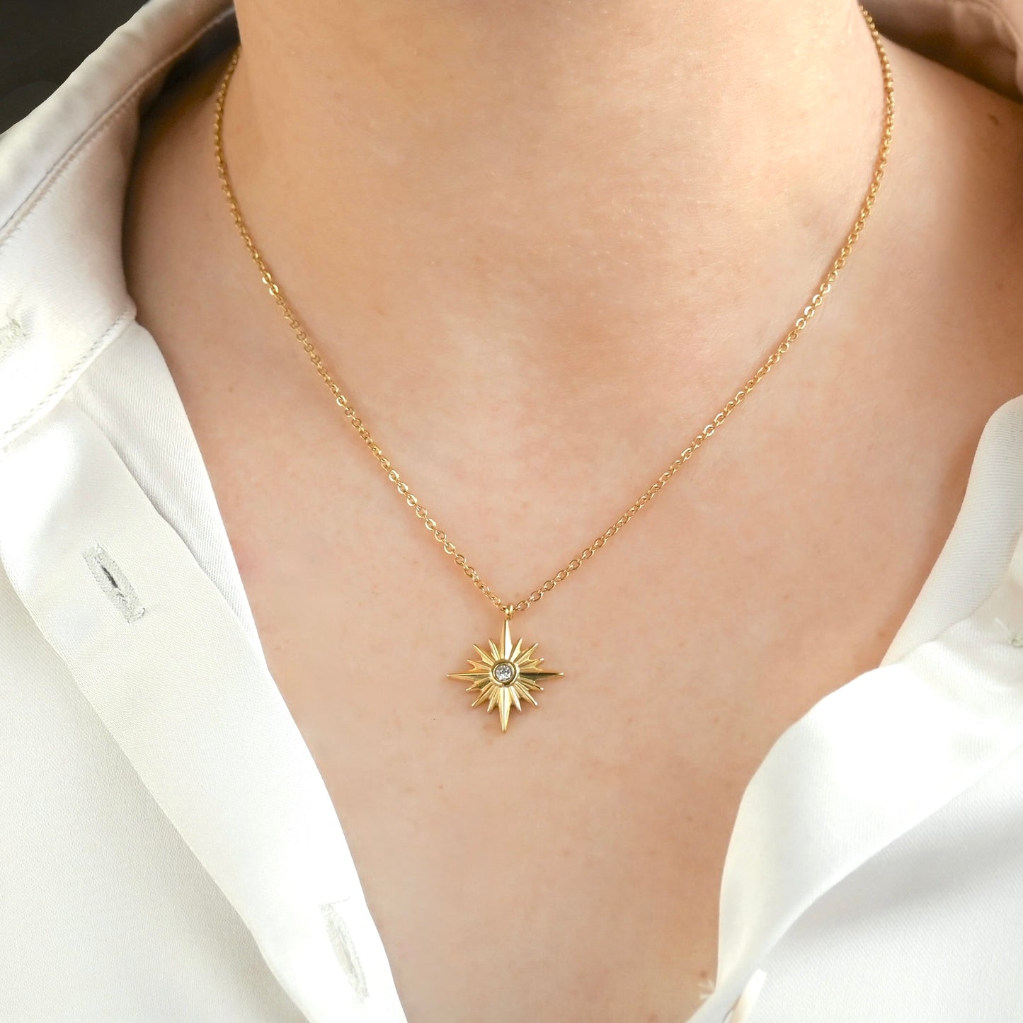 Gold necklace with a starburst medallion worn by a person in a white shirt.
