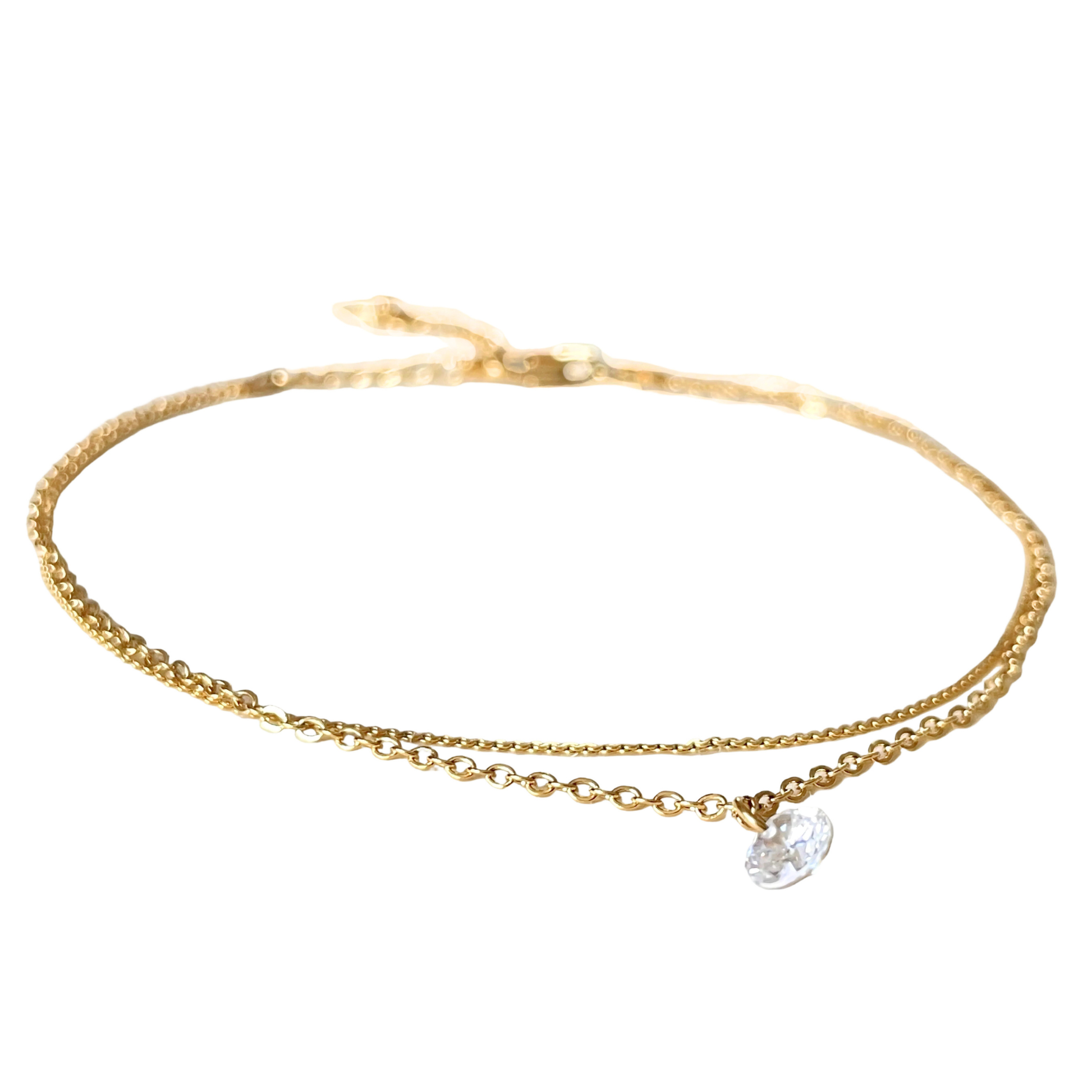 Delicate layered gold chain anklet with a tiny crystal charm hanging from its cable chain on a white background