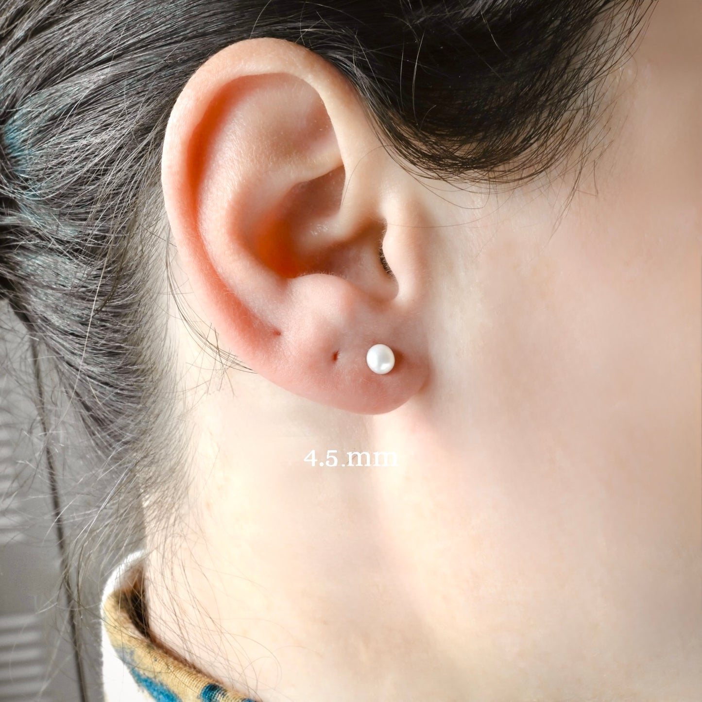 Close-up of an ear wearing a small 4mm pearl stud earrings with a blurred background