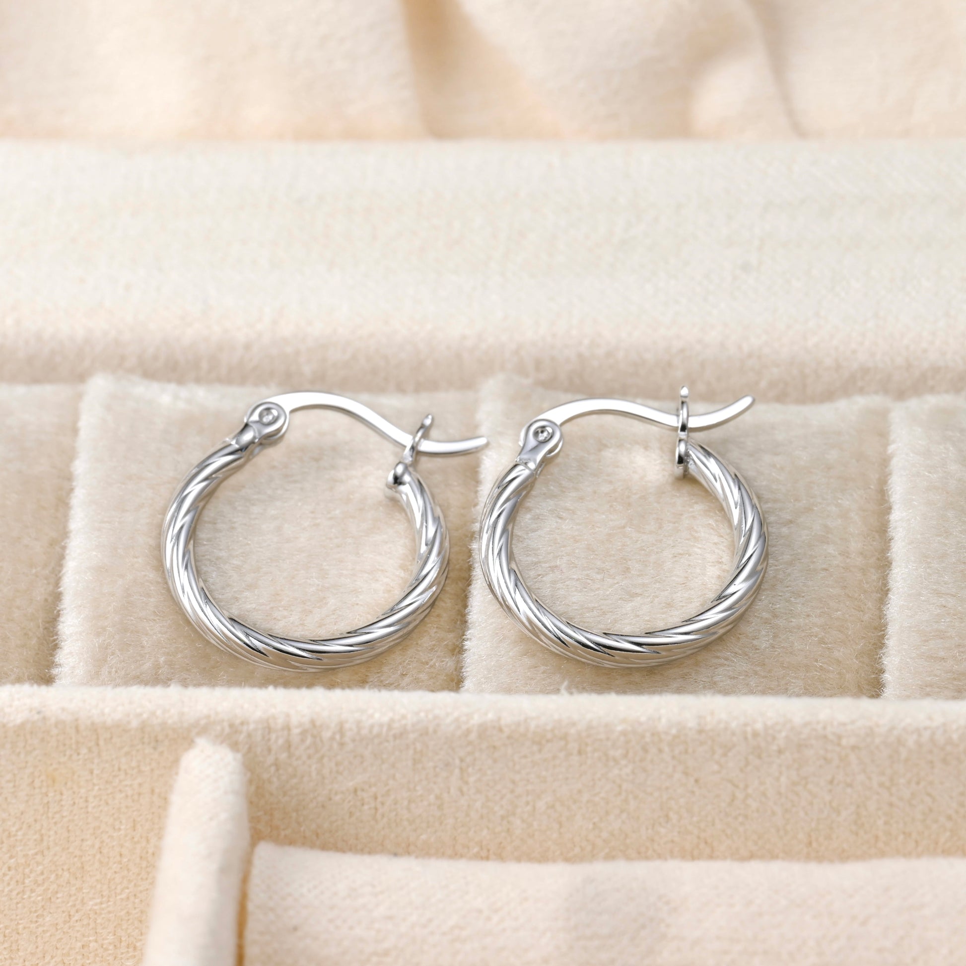 Pair of silver hoop earrings on a beige jewelry box