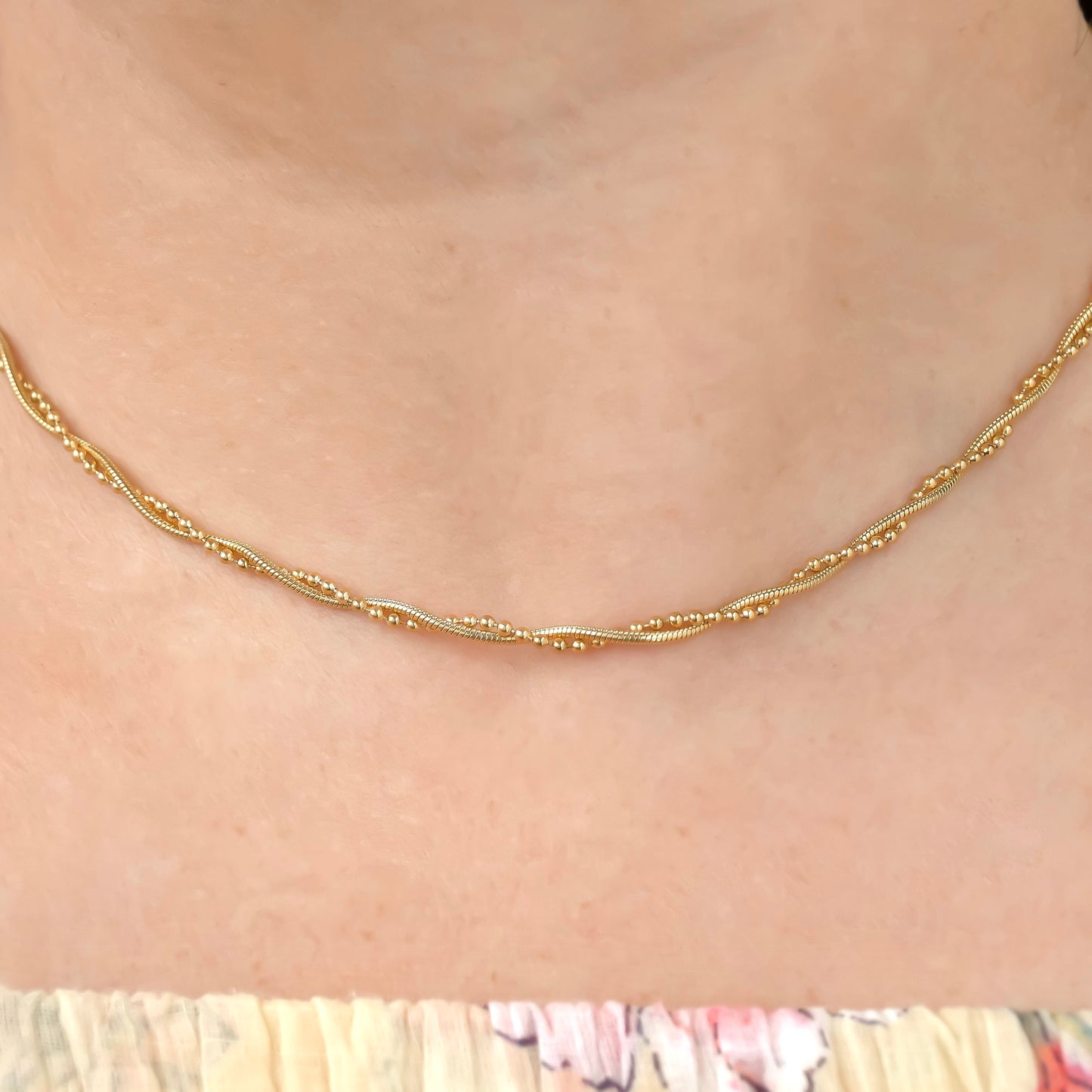 close up front view of twisted Gold snake chain necklace on a person with a blurred background
