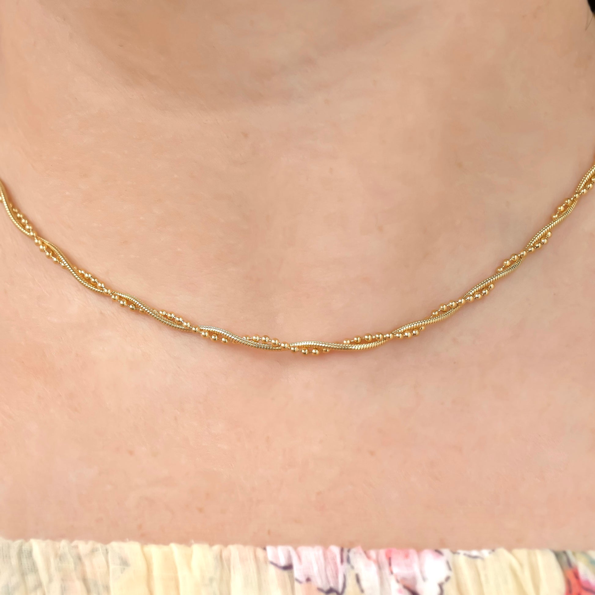 close up front view of twisted Gold snake chain necklace on a person with a blurred background