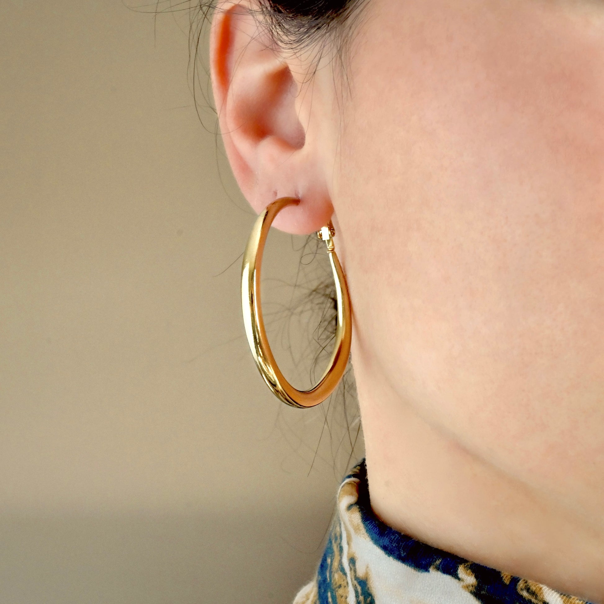 Front-view of thick gold hoop earrings worn by a person with a neutral background
