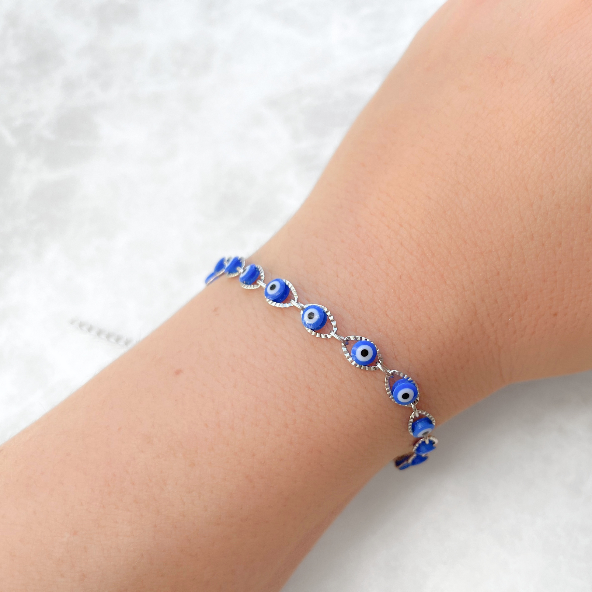 Silver bracelet with blue evil eye beads on a person's wrist against a white background