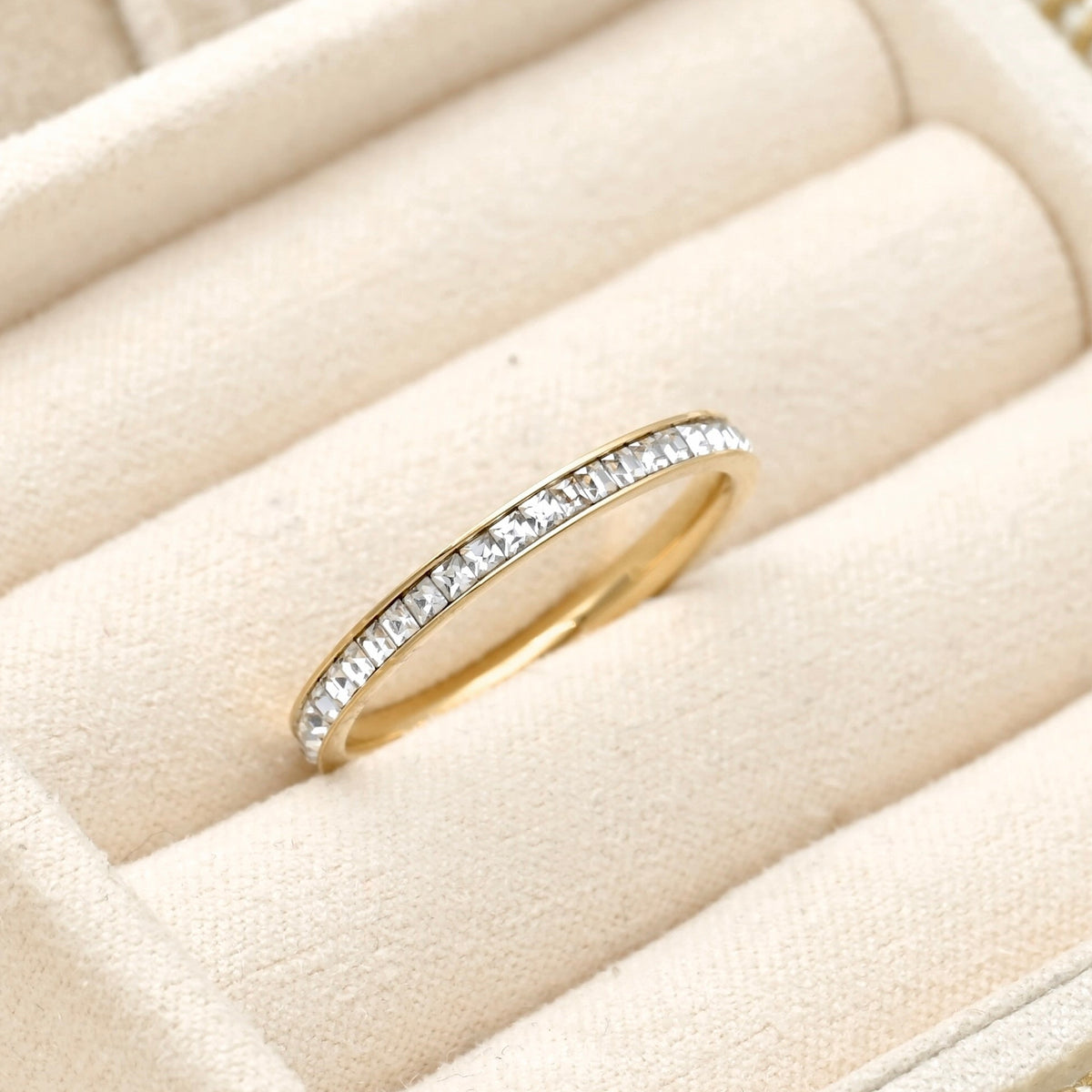 Slim gold eternity ring with channel set squre cubic zirconia stones in a beige jewelry box