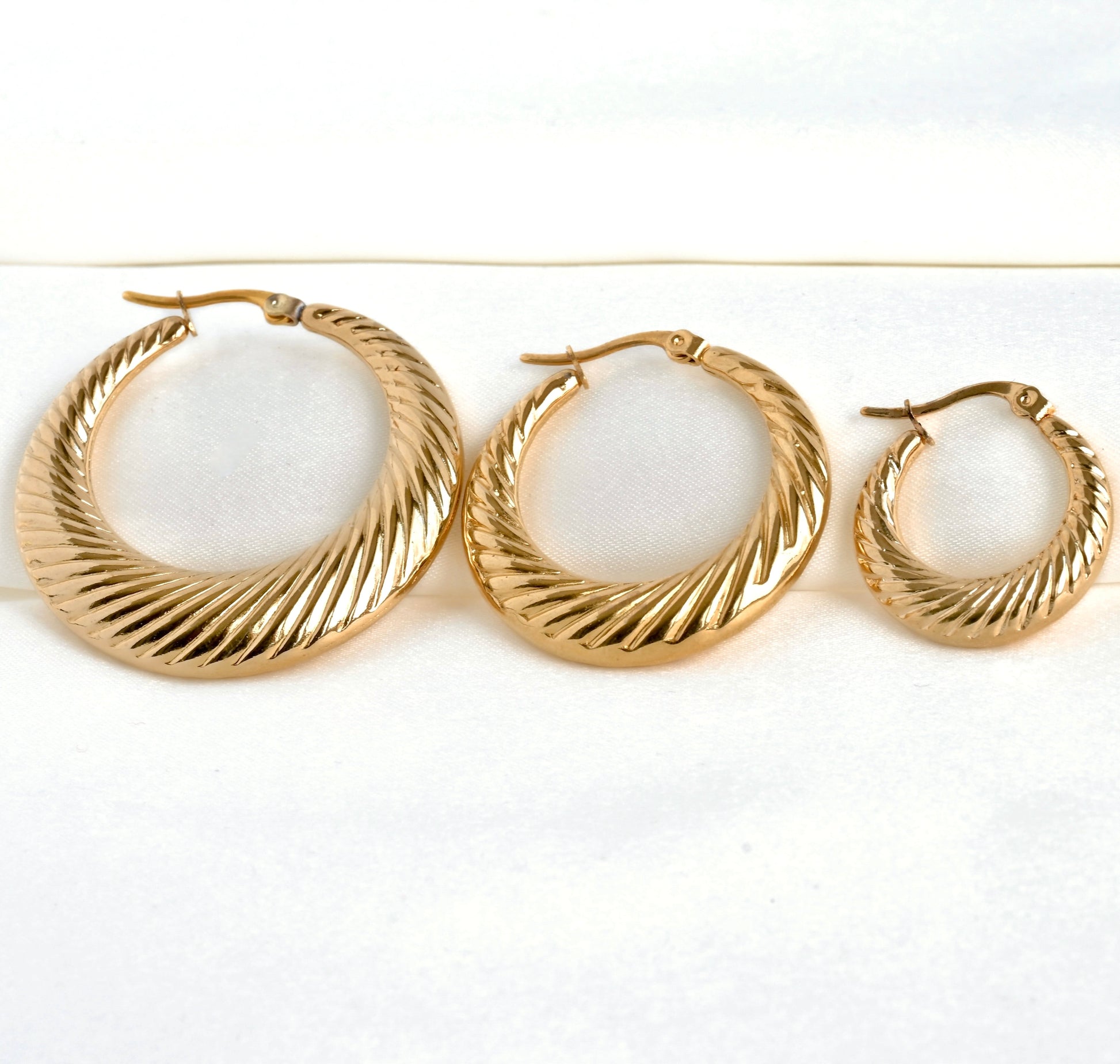 Three gold hoop earrings in three different sizes on a white background