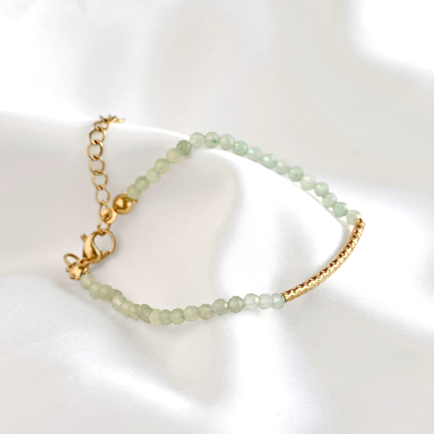 Green beaded bracelet with gold chain on a white background