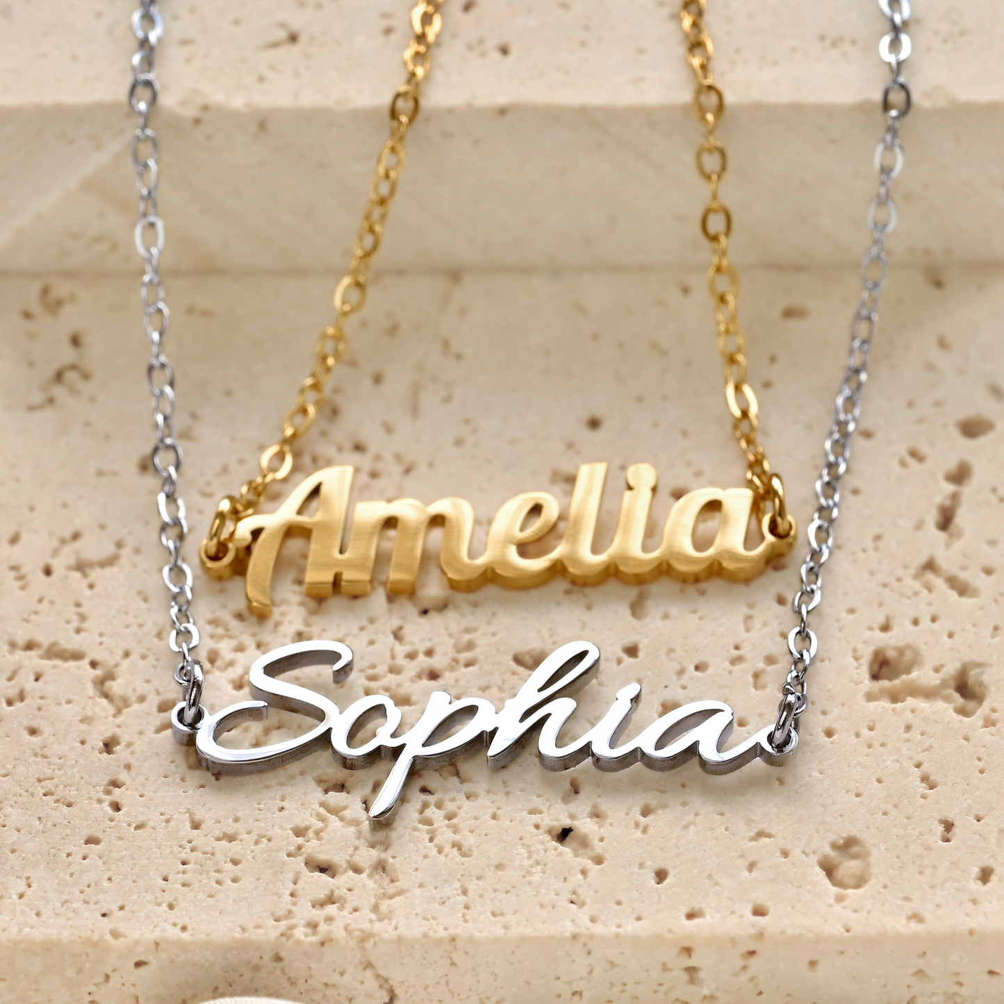 Gold and silver name bracelets on a textured beige surface