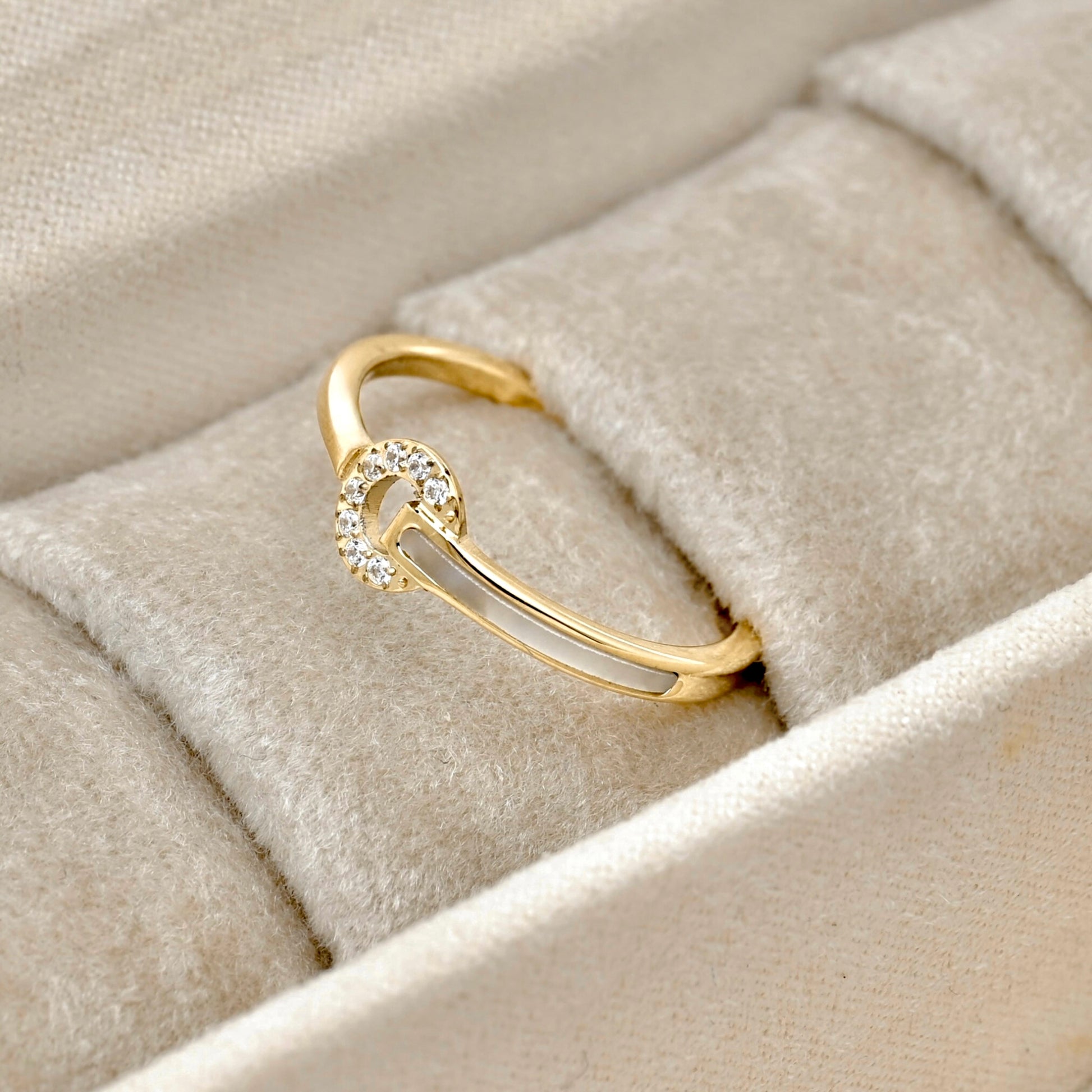 Gold circle ring adorned with cz stones and shell inlay on one side of the band, displayed in a beige jewelry box.